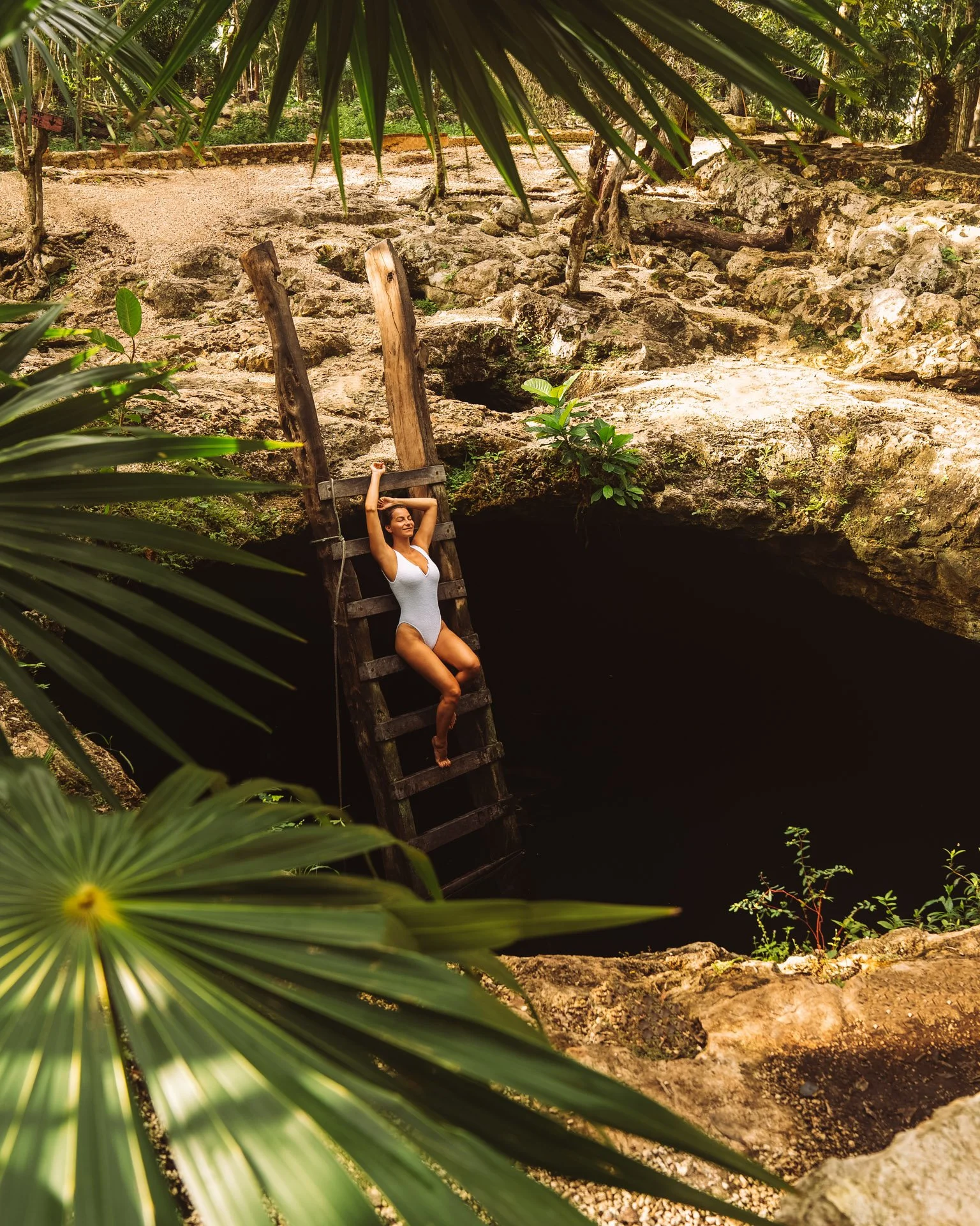 Woman in white swimsuit on wooden ladder over cenote