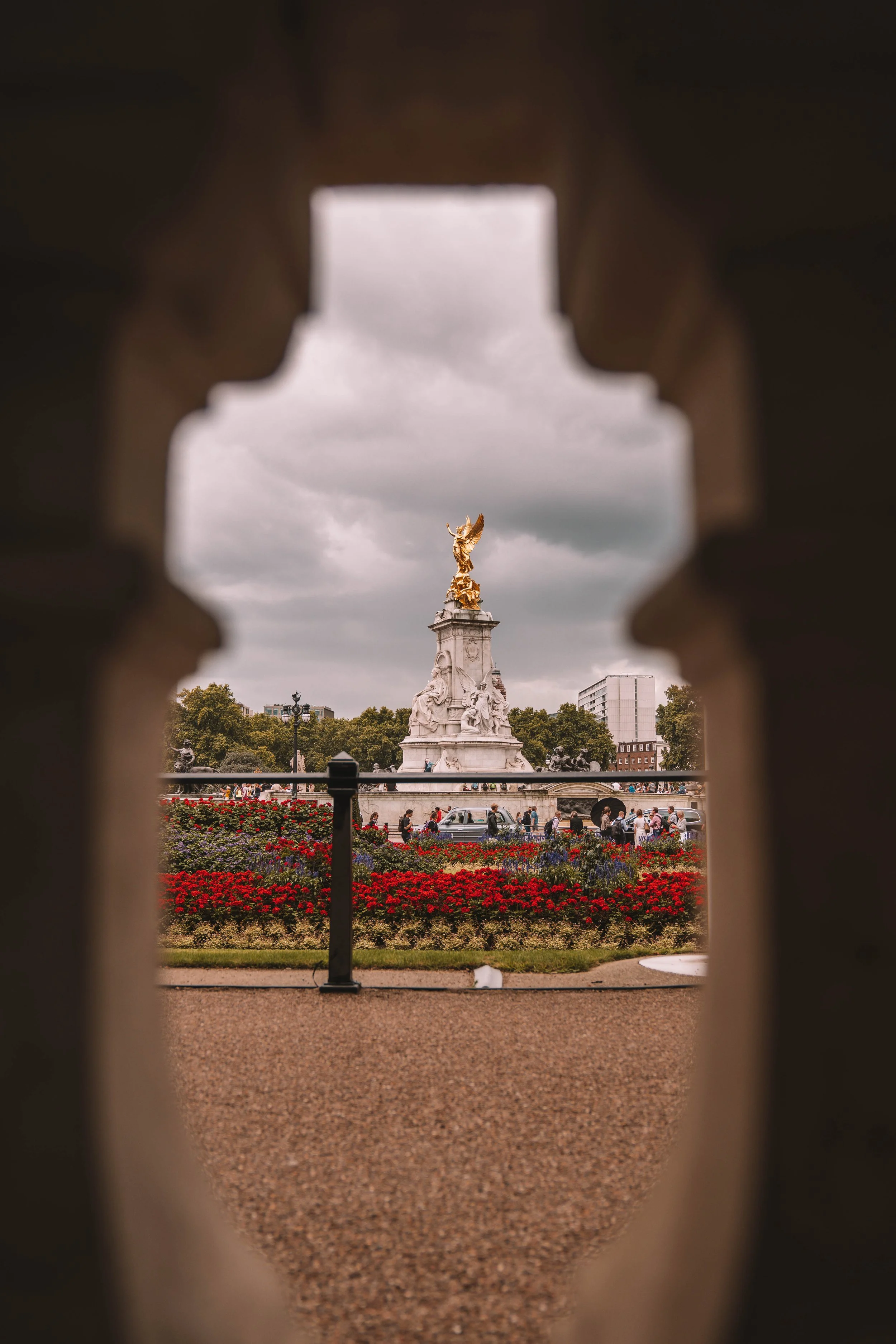 View of the Victoria Memorial statue with a golden figure on top, surrounded by red flowers and people, seen through an archway.