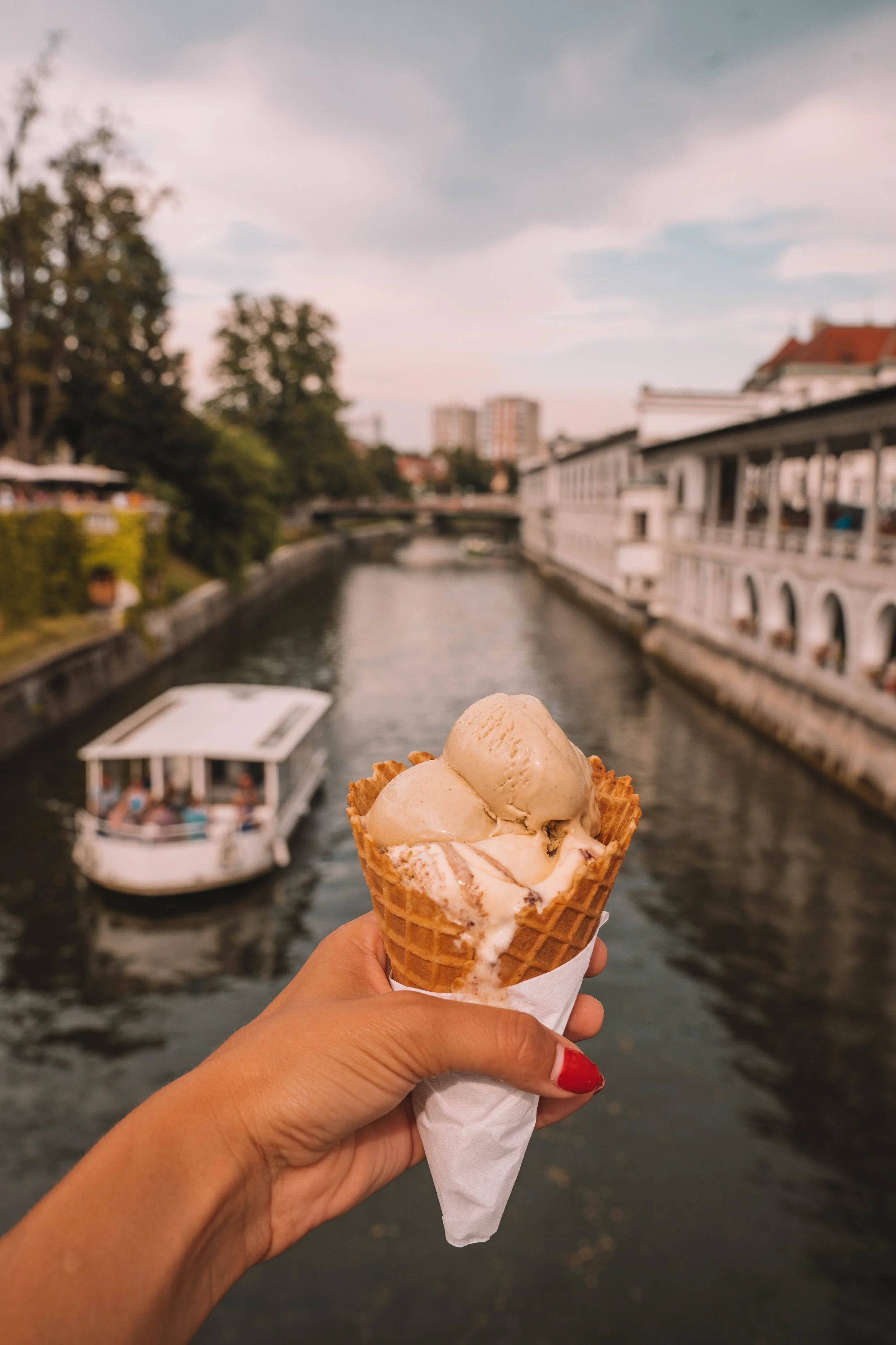 Hand holding an ice cream cone with a river and boat in the background.