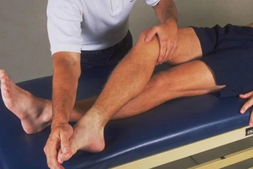 A physical therapist working on a patient's leg while laying on a treatment table.