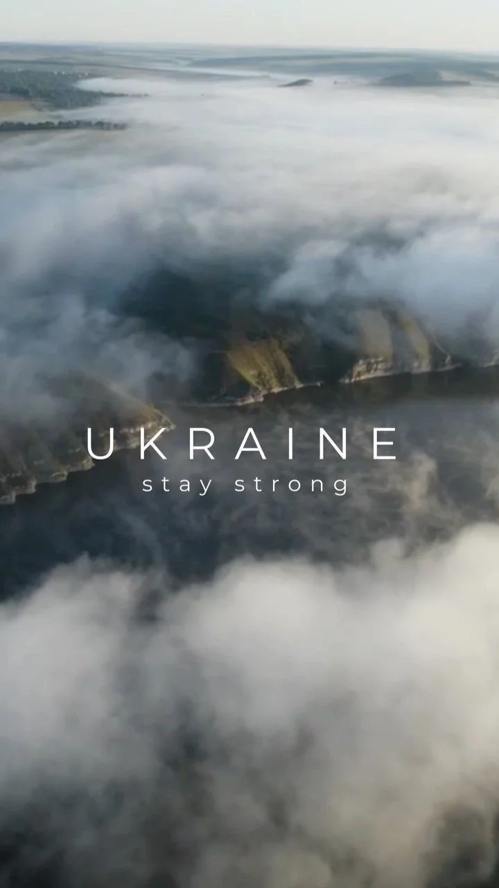 Aerial view of a landscape with smoke and clouds over a river or lake, with the text 'Ukraine stay strong' displayed.