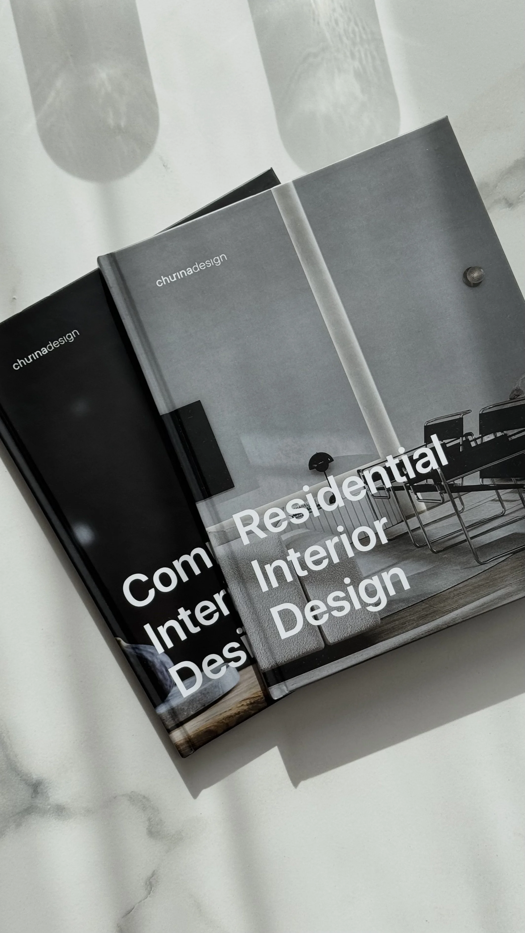 Books titled 'Community Residential Interior Design' by Churned Design on a white surface with shadows.