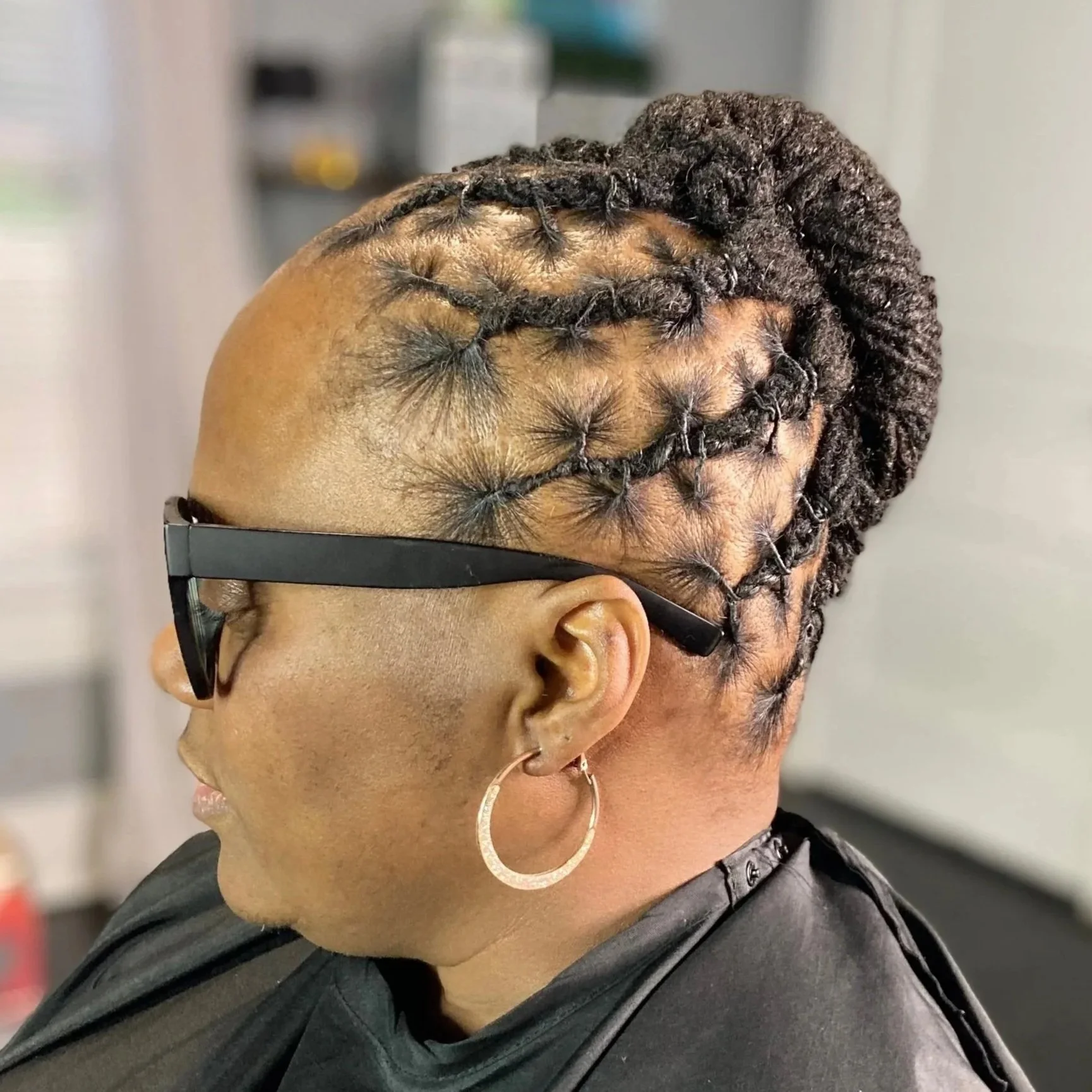 A woman with glasses and hoop earrings showcasing a hairstyle involving cornrows and twists.
