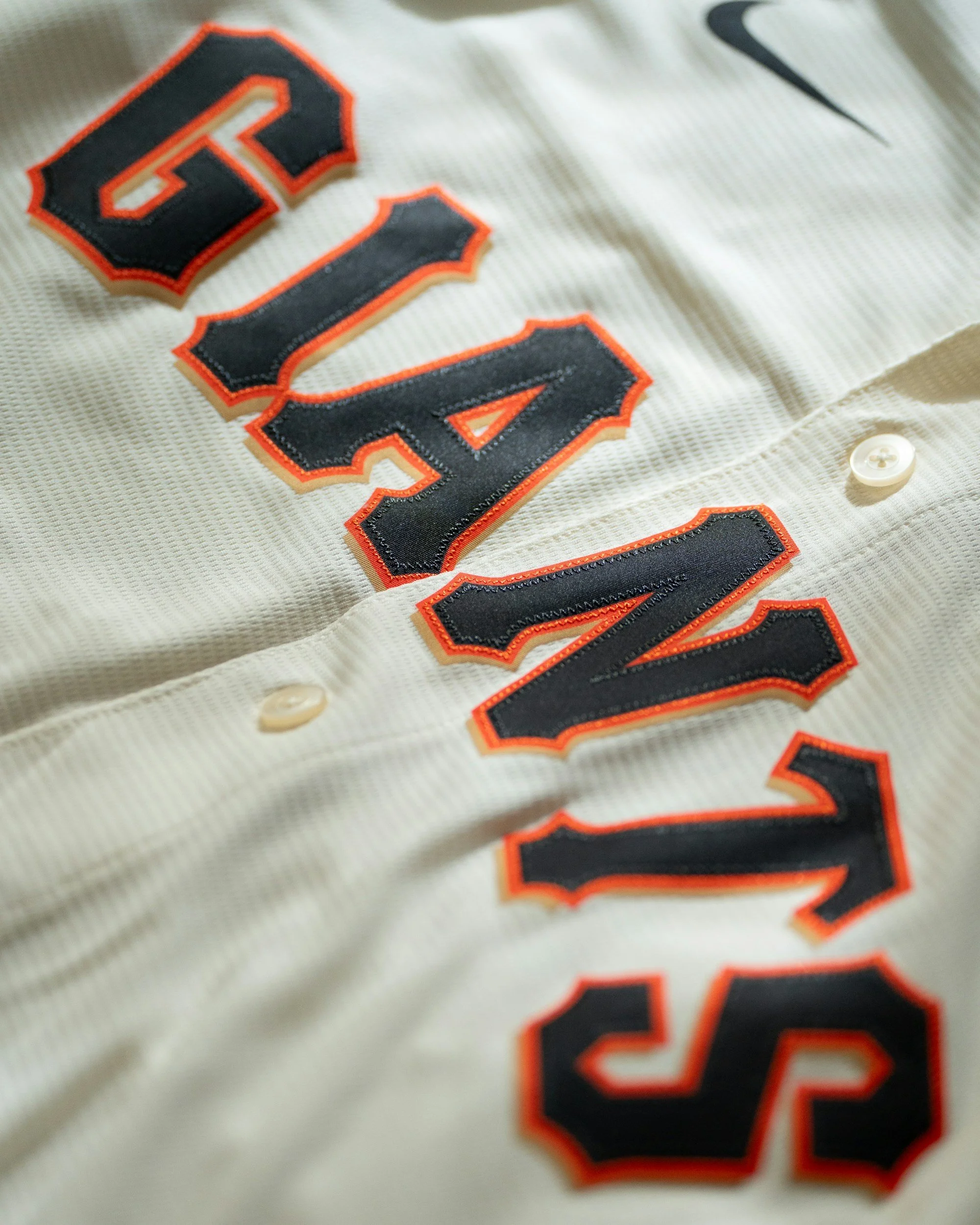 Close-up of a baseball jersey with embroidered black and orange numbers and black Nike swoosh logo.