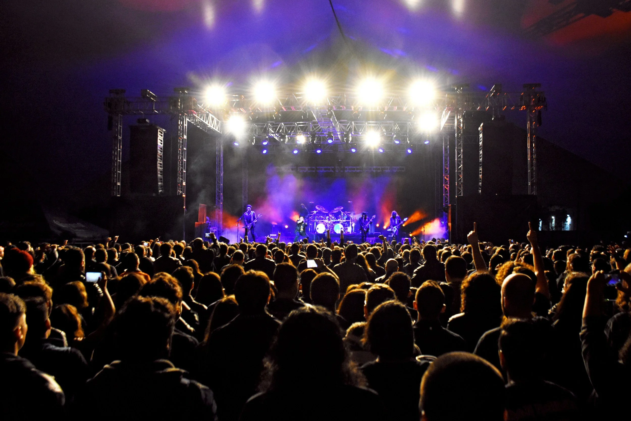 A large crowd attending a concert with a band performing on stage under bright lights.
