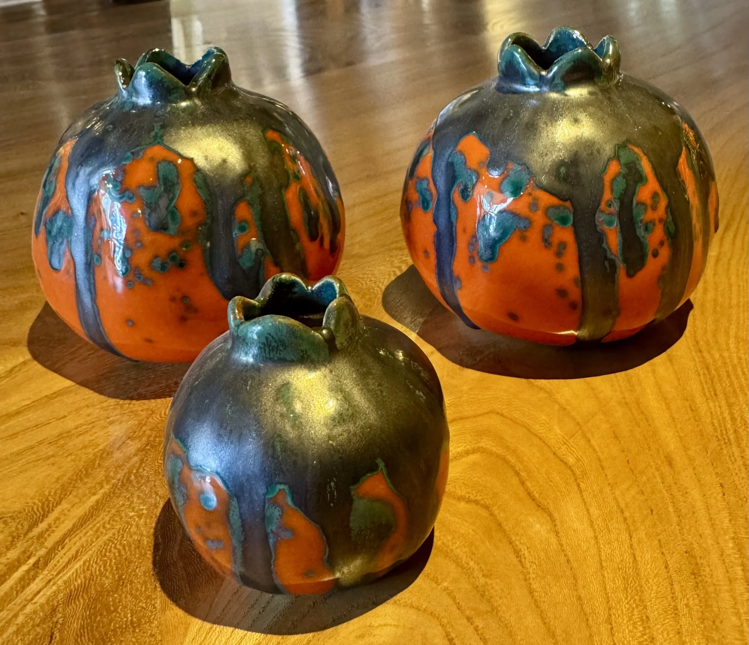Decorative ceramic pomegranates of various sizes, with a colorful glaze, arranged on a wooden surface.