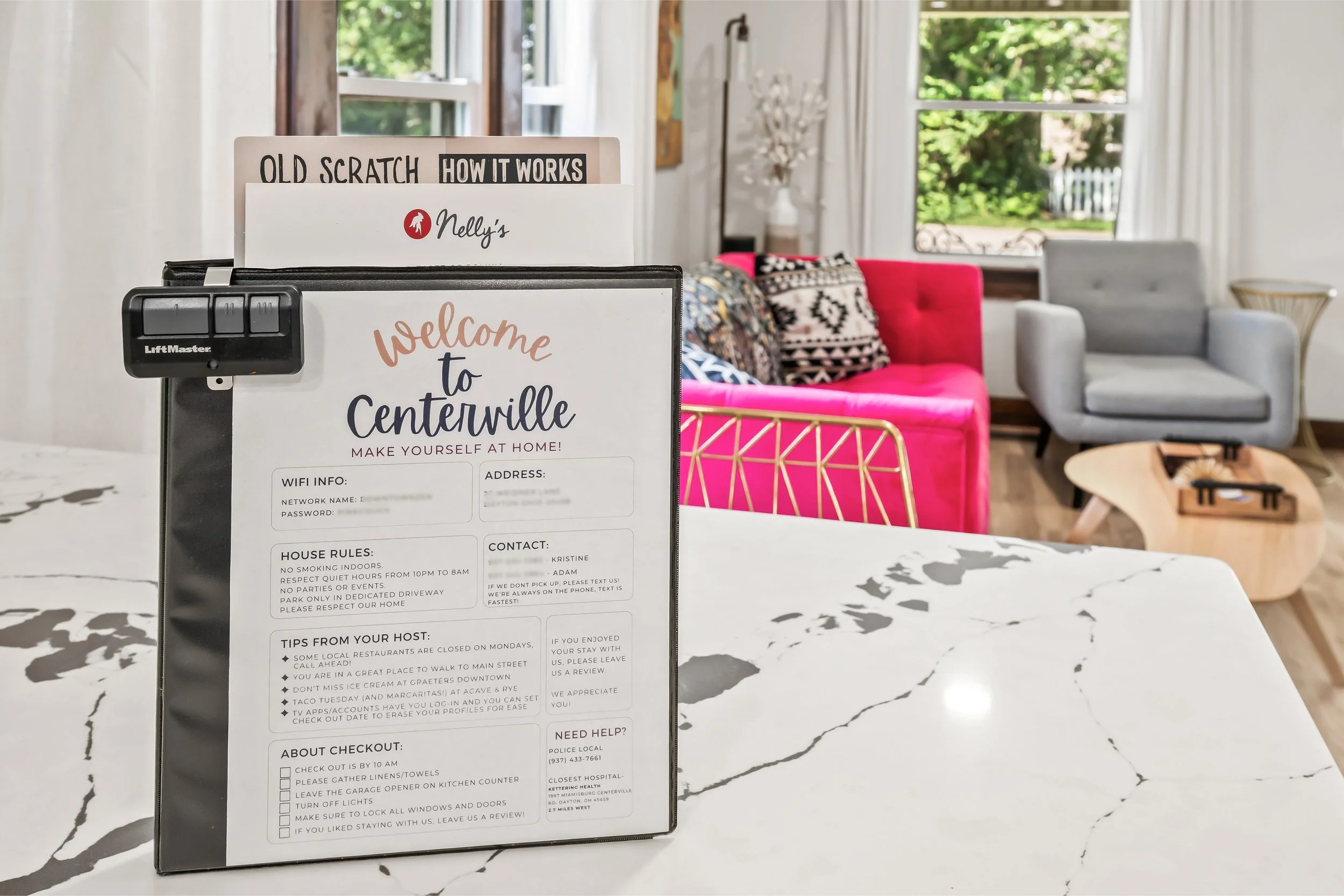 A welcome sign for Centerville placed on a marble countertop, with a pink velvet sofa and patterned pillows in the background in a bright living room with large windows and greenery outside.