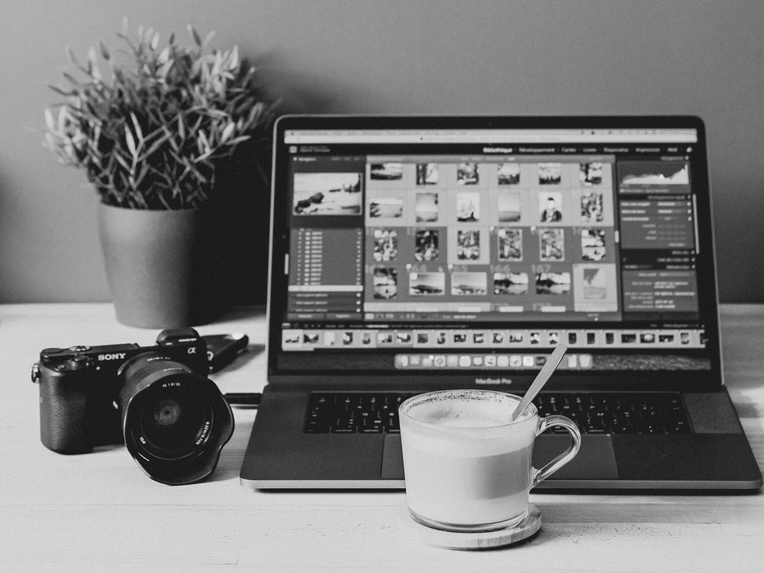 A black and white image of a desk with a camera and a computer with Photoshop.