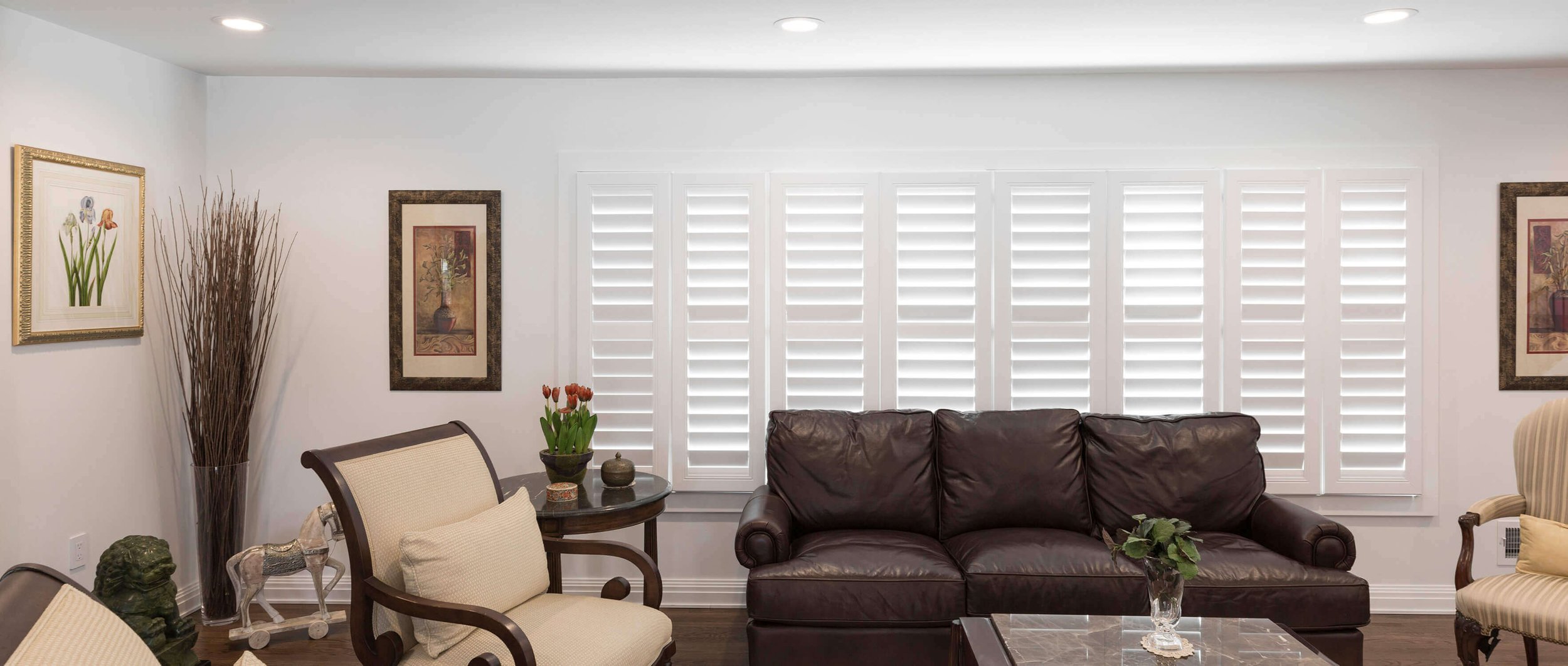 A living room with leather furniture and a large window with white shutters about energy efficiency and uv protection