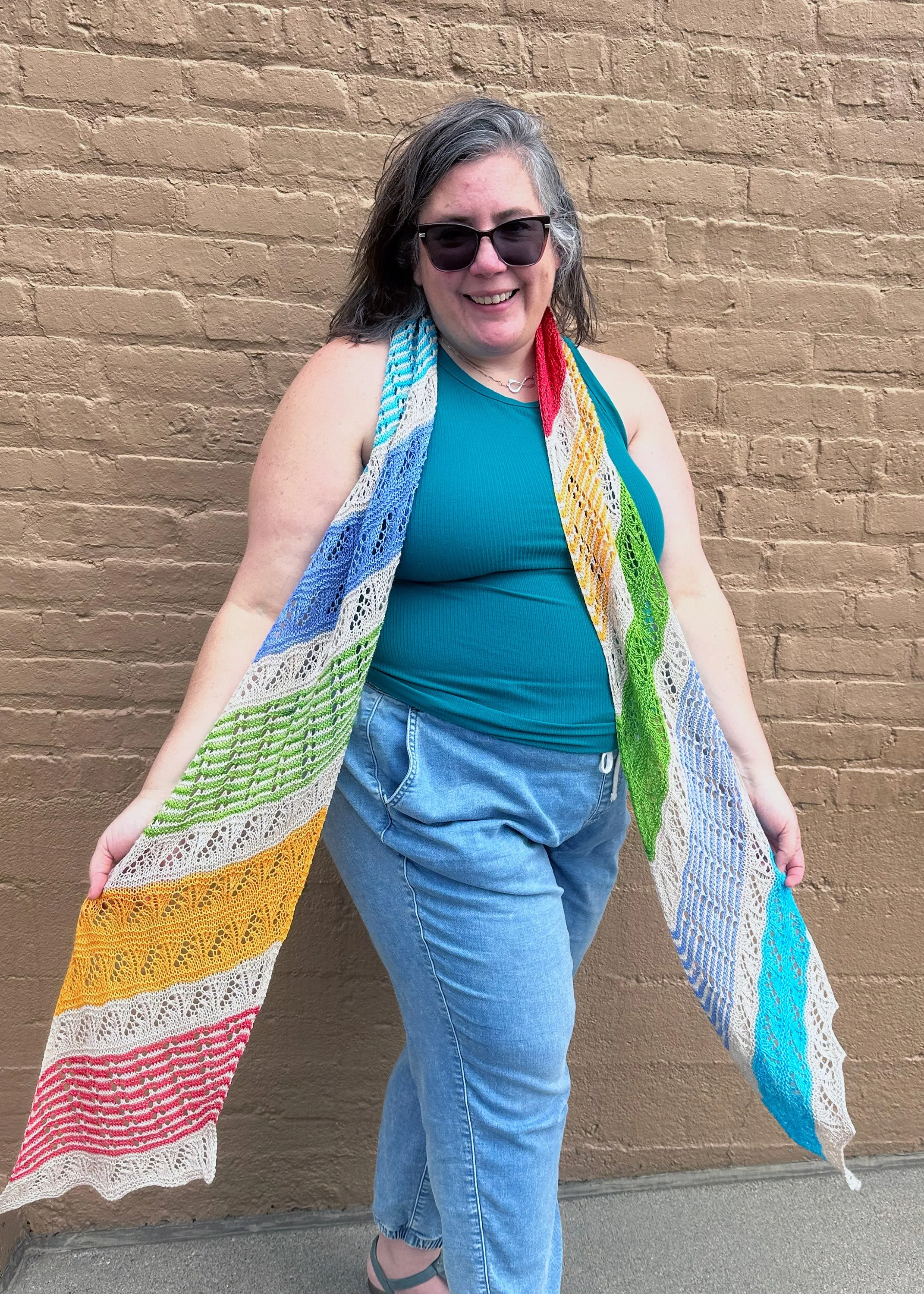 Long rainbow colored scarf modeled in front of a brick wall.