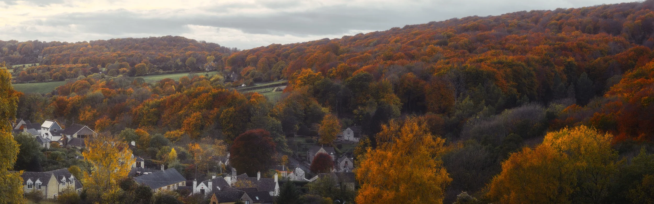 Autumn coloured trees surround a small Cotswold village situated at the bottom of a valley near Gloucester