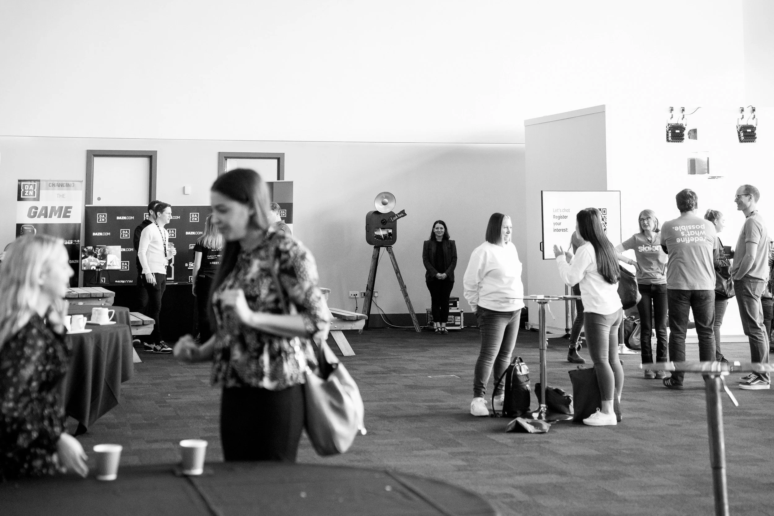 People networking at a conference with banners and a vintage camera prop in the background, black and white photo.