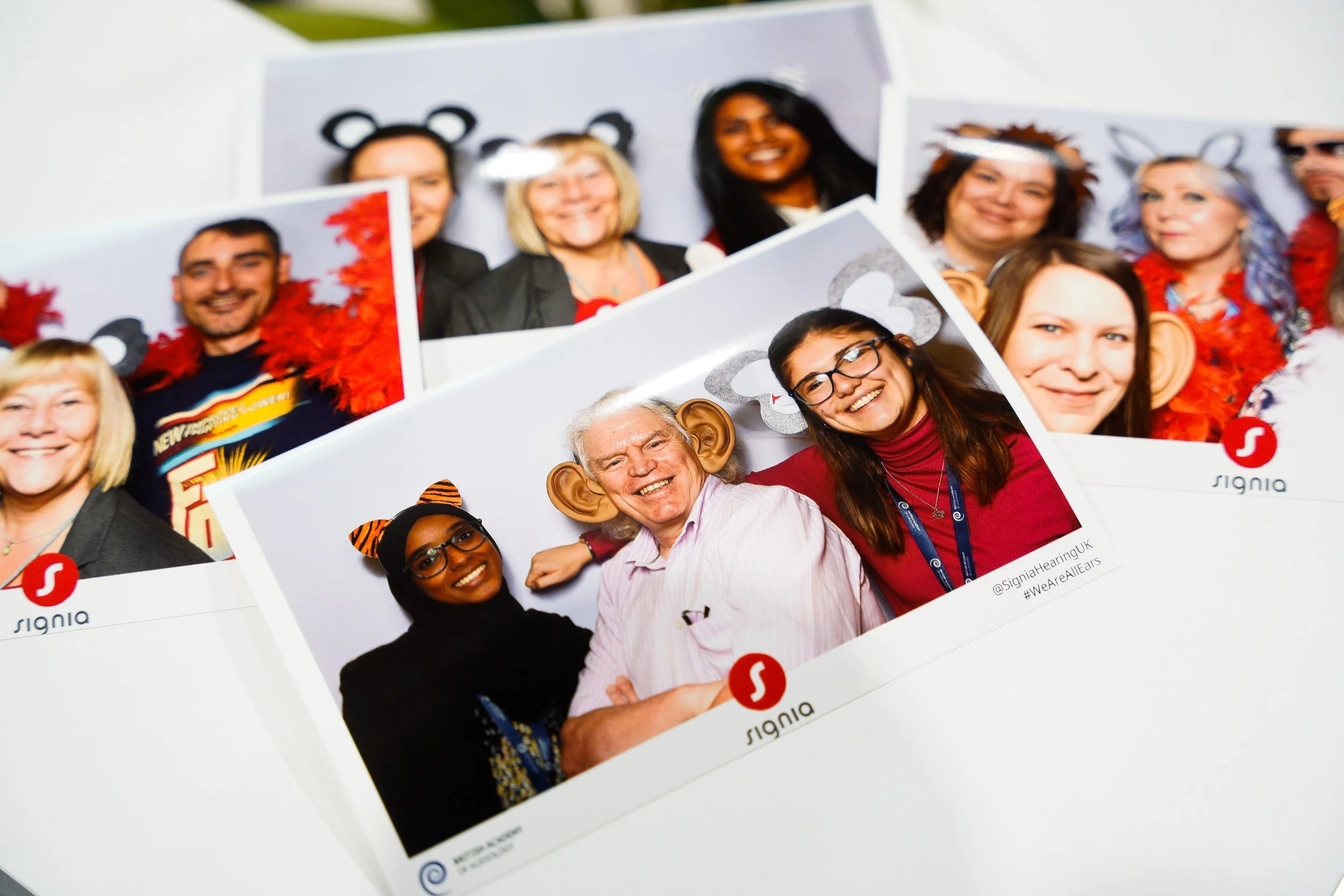 Group of people wearing animal ears costumes and red feather boas at a photo booth during an event.