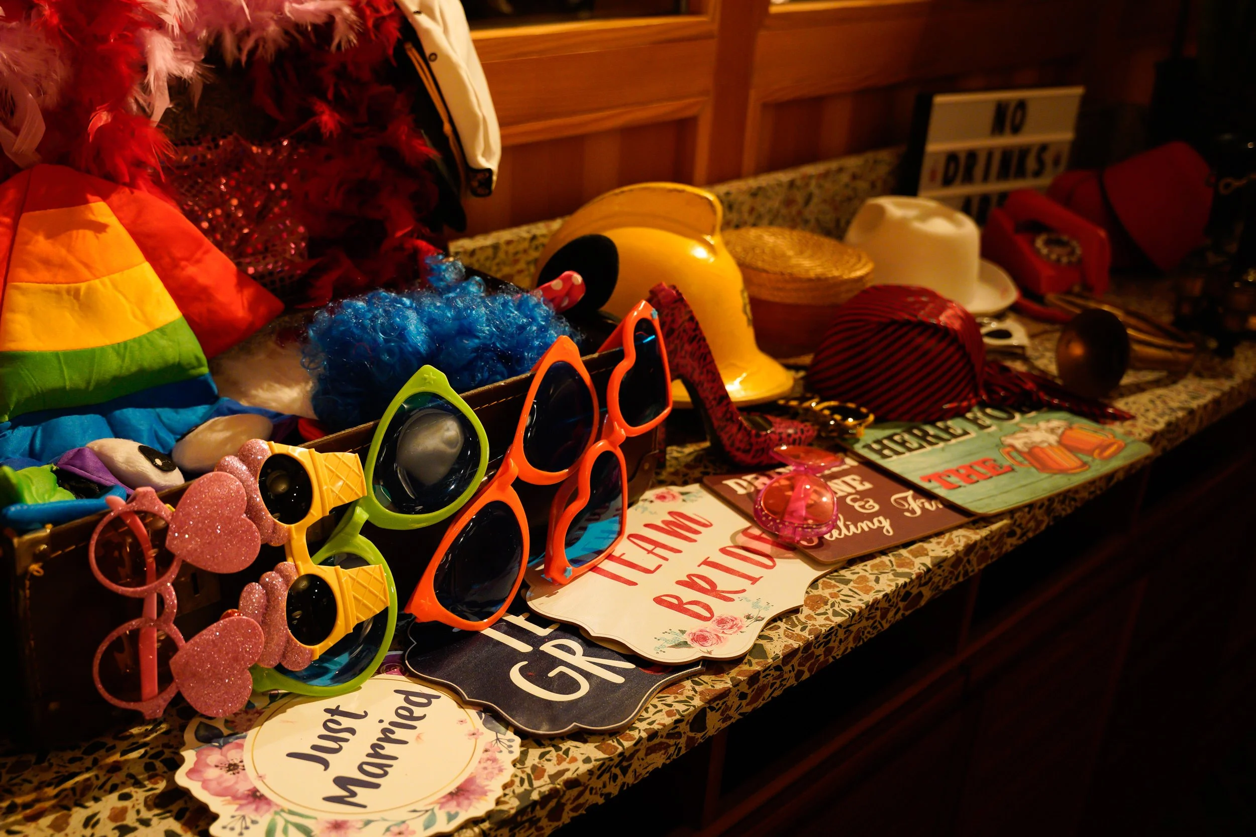 A collection of colorful accessories and signs on a countertop, including sunglasses, hats, signs with wedding and marriage messages, and decorative items.