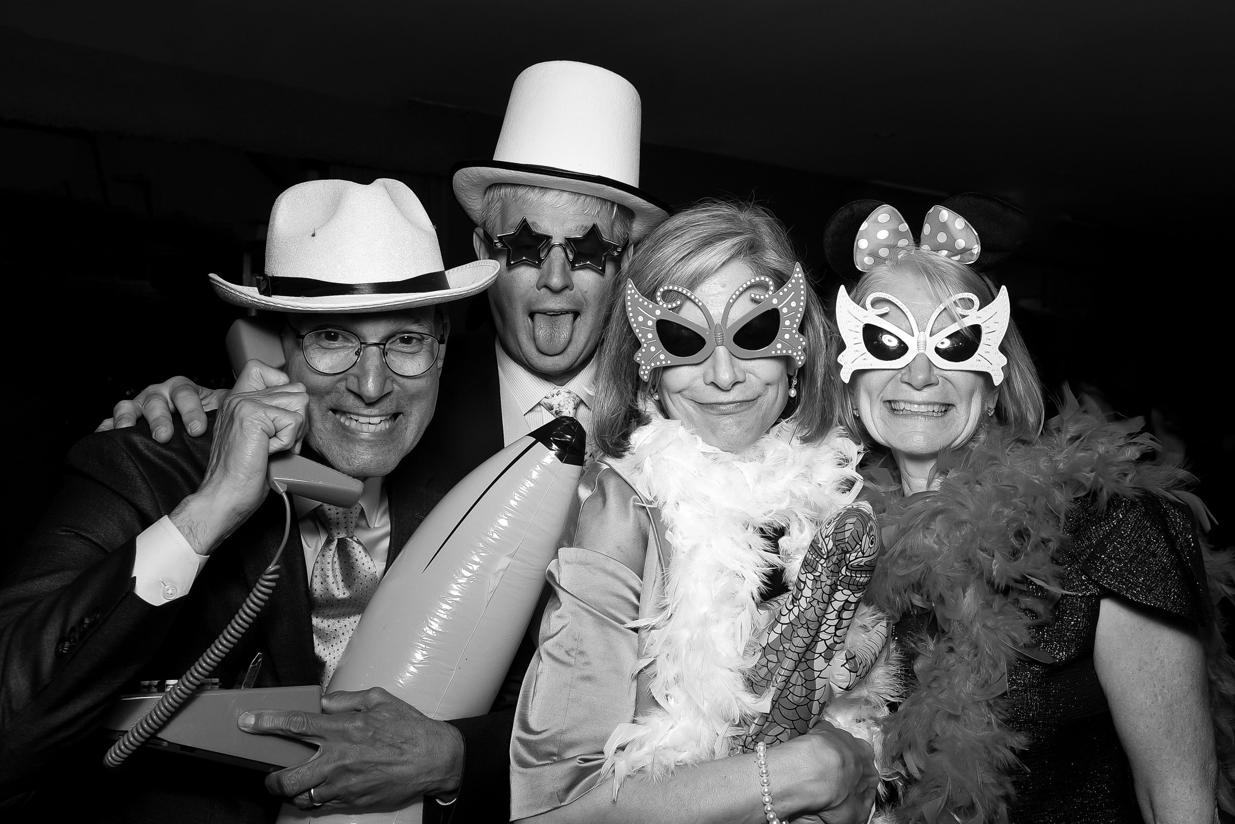 Four adults wearing funny costumes and masks at a party, with one on the phone, all smiling and having fun.