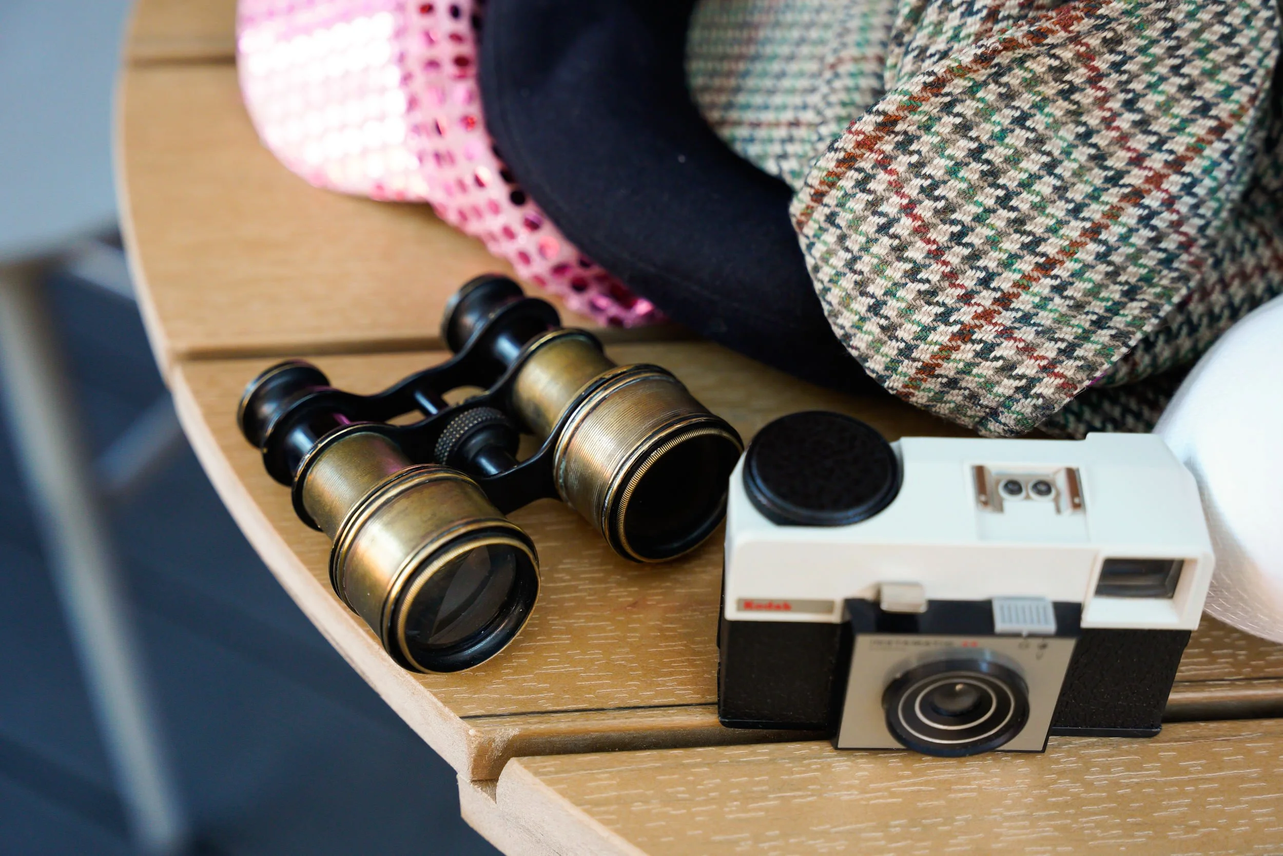 Vintage Kodak camera, binoculars, and various fabric pieces on a wooden table.