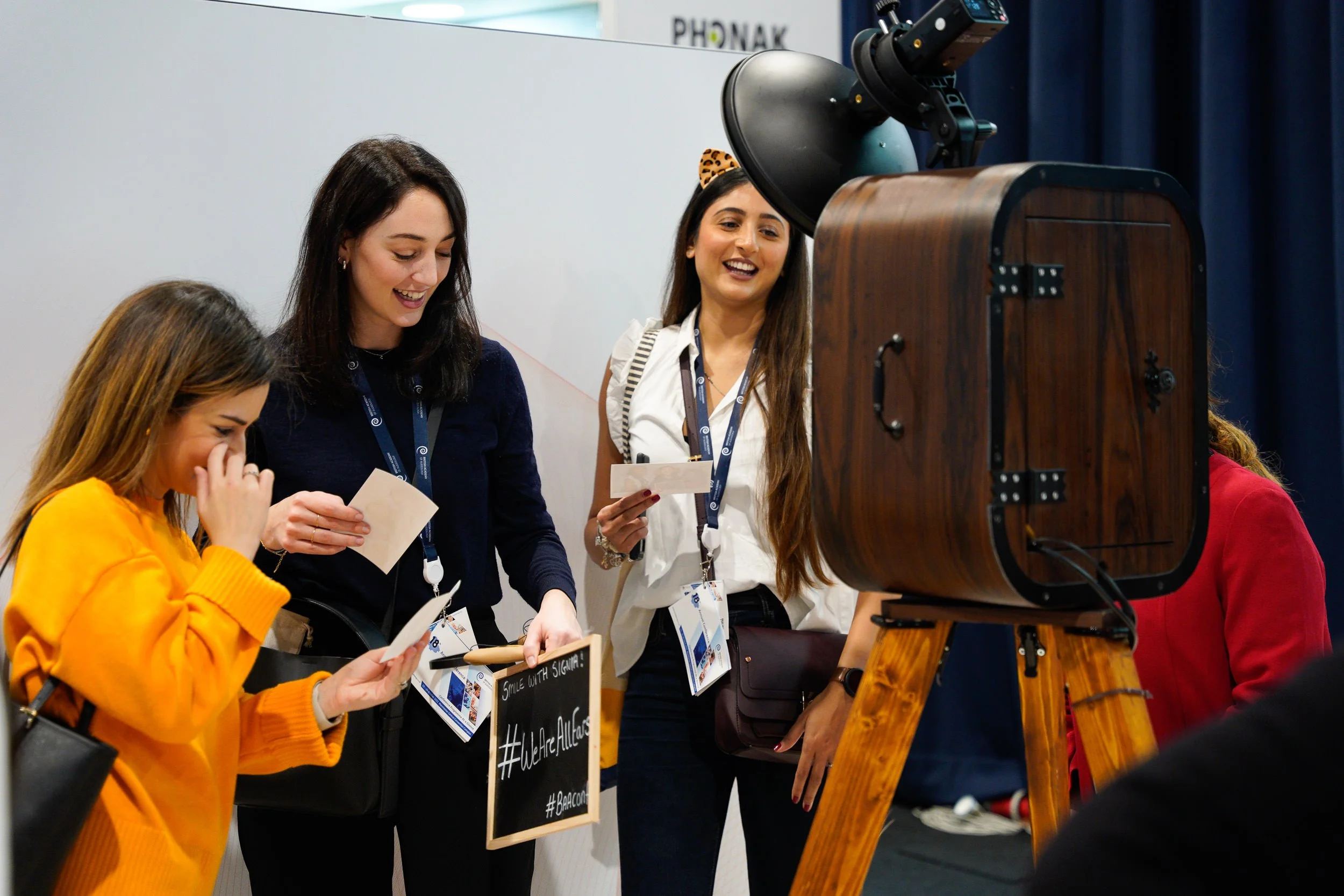 Group of women at a photo booth with a vintage camera, smiling and taking pictures during an event.