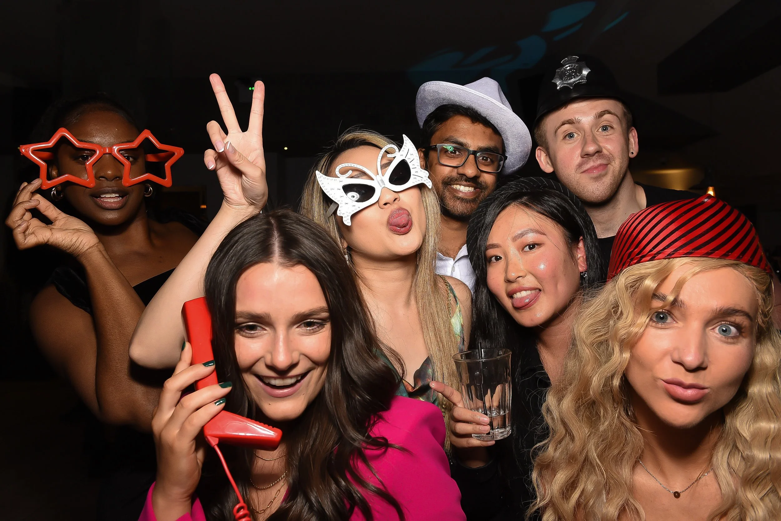 Group of friends at a party wearing fun and colorful costumes and accessories, making silly faces and posing for the camera.