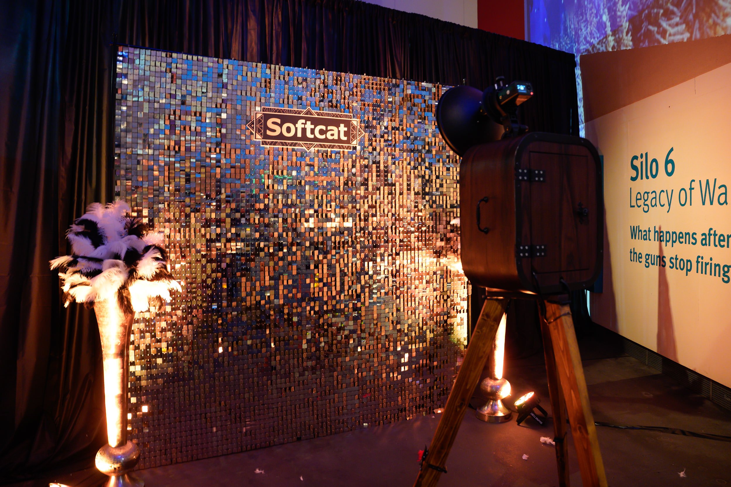 Decorative backdrop with a sign reading "Softcat" and a palm tree with white and black feathers, additional lighting and screen projection on the right side.