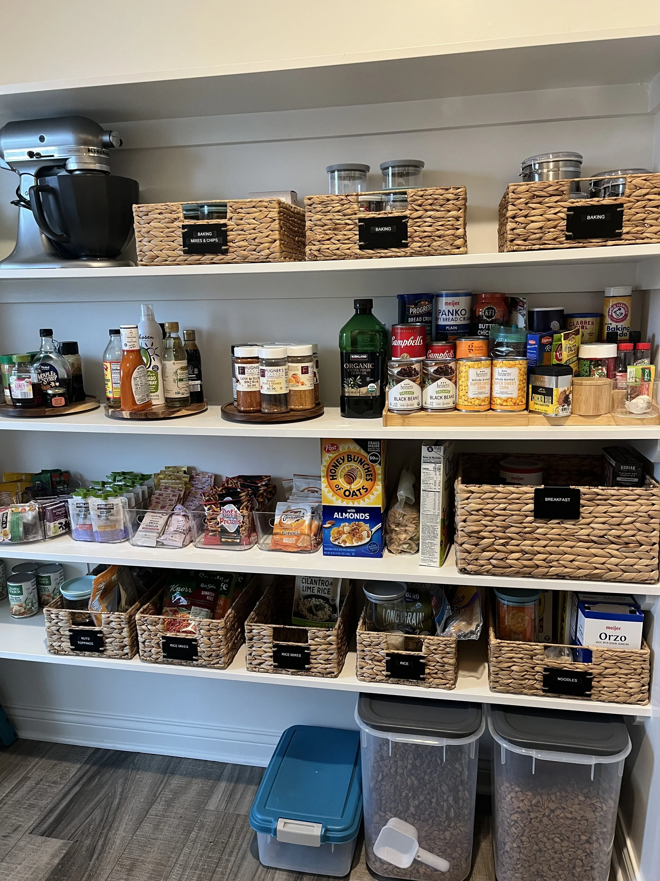 Straight on view of pantry shelves holding matching baskets of food, dog food at the bottom and lazy susans, very organized