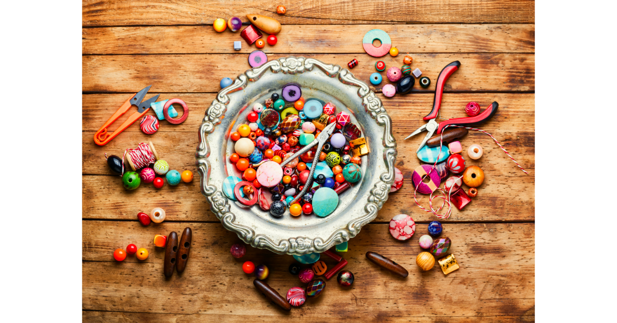 decorative bowl filled with beads along with some colorful beads sprinkled around it on the wooden table as well as some jewelry making tools mixed in as well