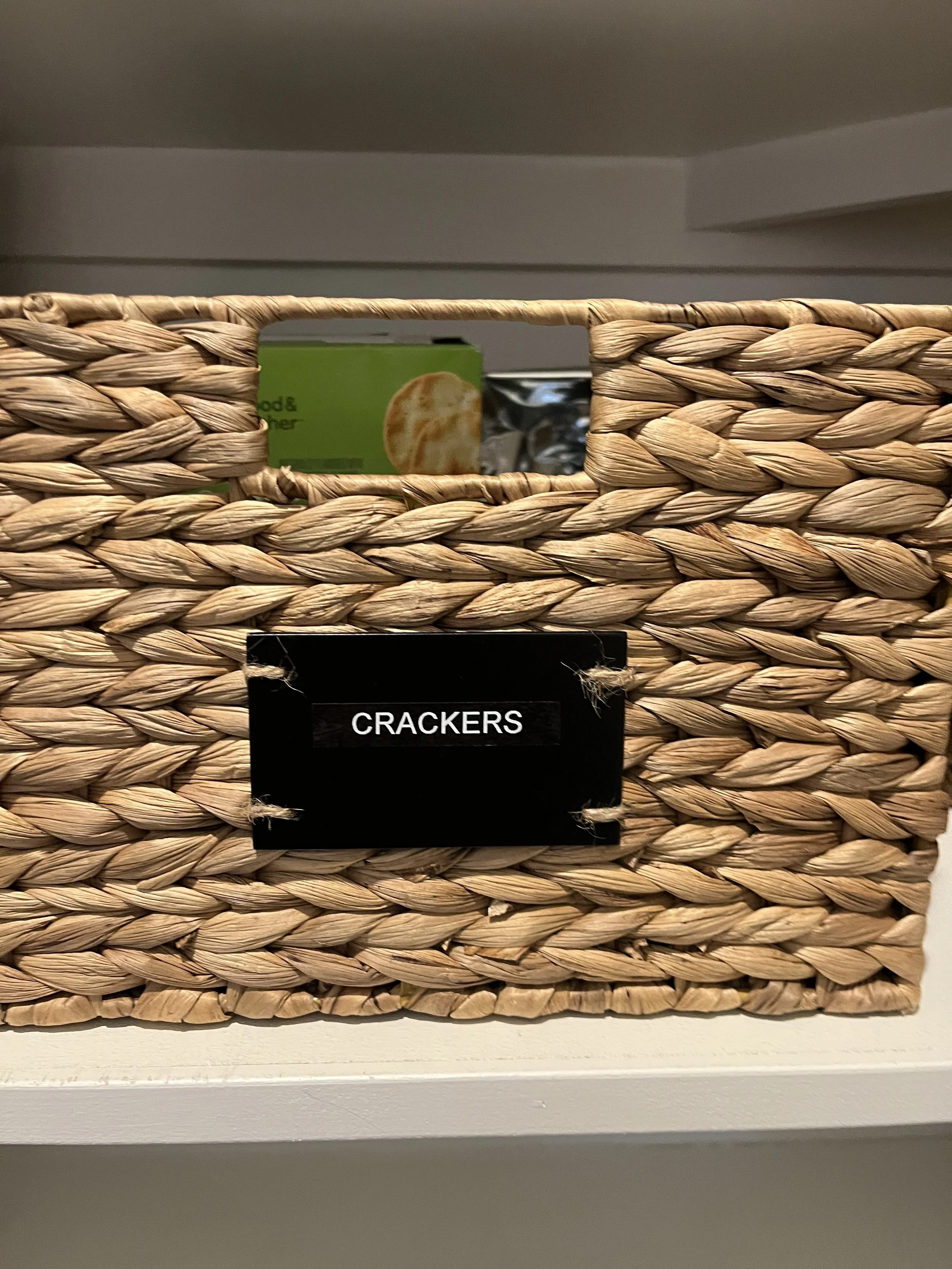 Detail of a natural color wicker pantry basket with a black label with white writing that says "crackers"