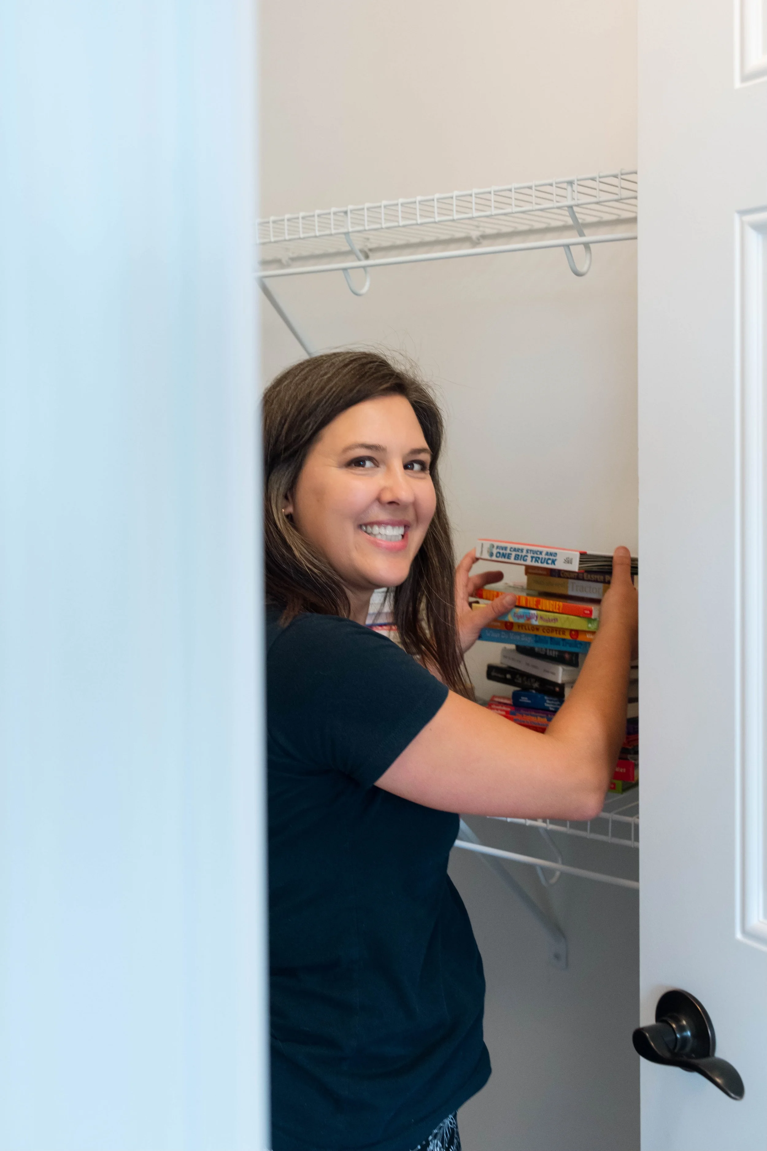 Devon smiling at the camera tidying a stack of books in the closet