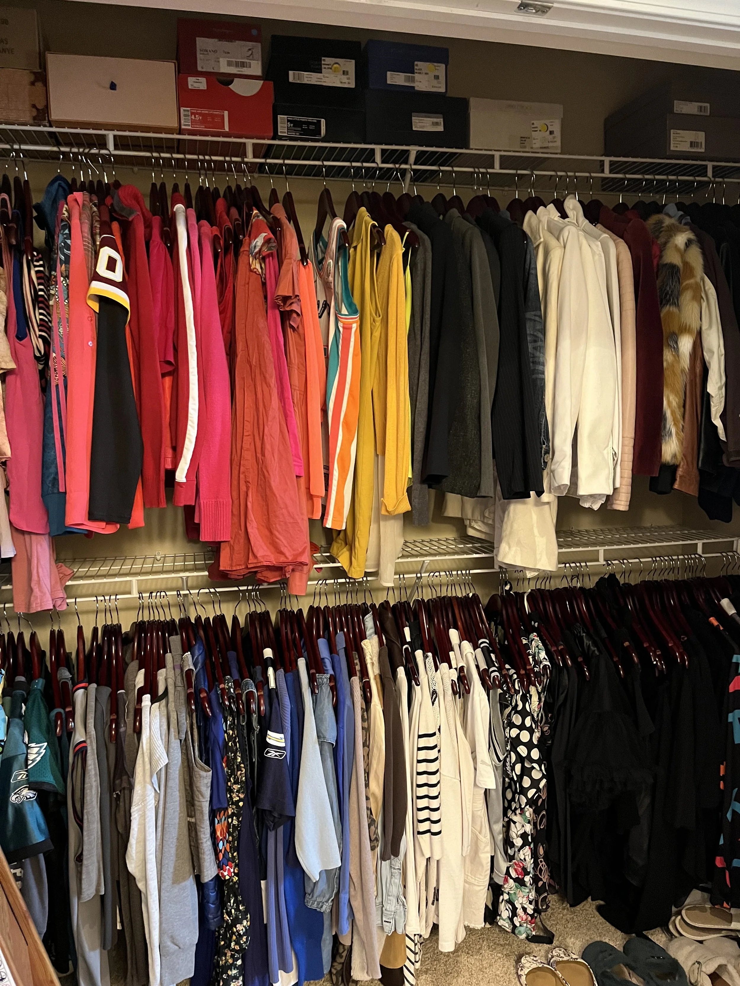 Tidy closet with double hanging bars, all items are hanging neatly and sorted by color and style with shoeboxes neatly on the top shelf
