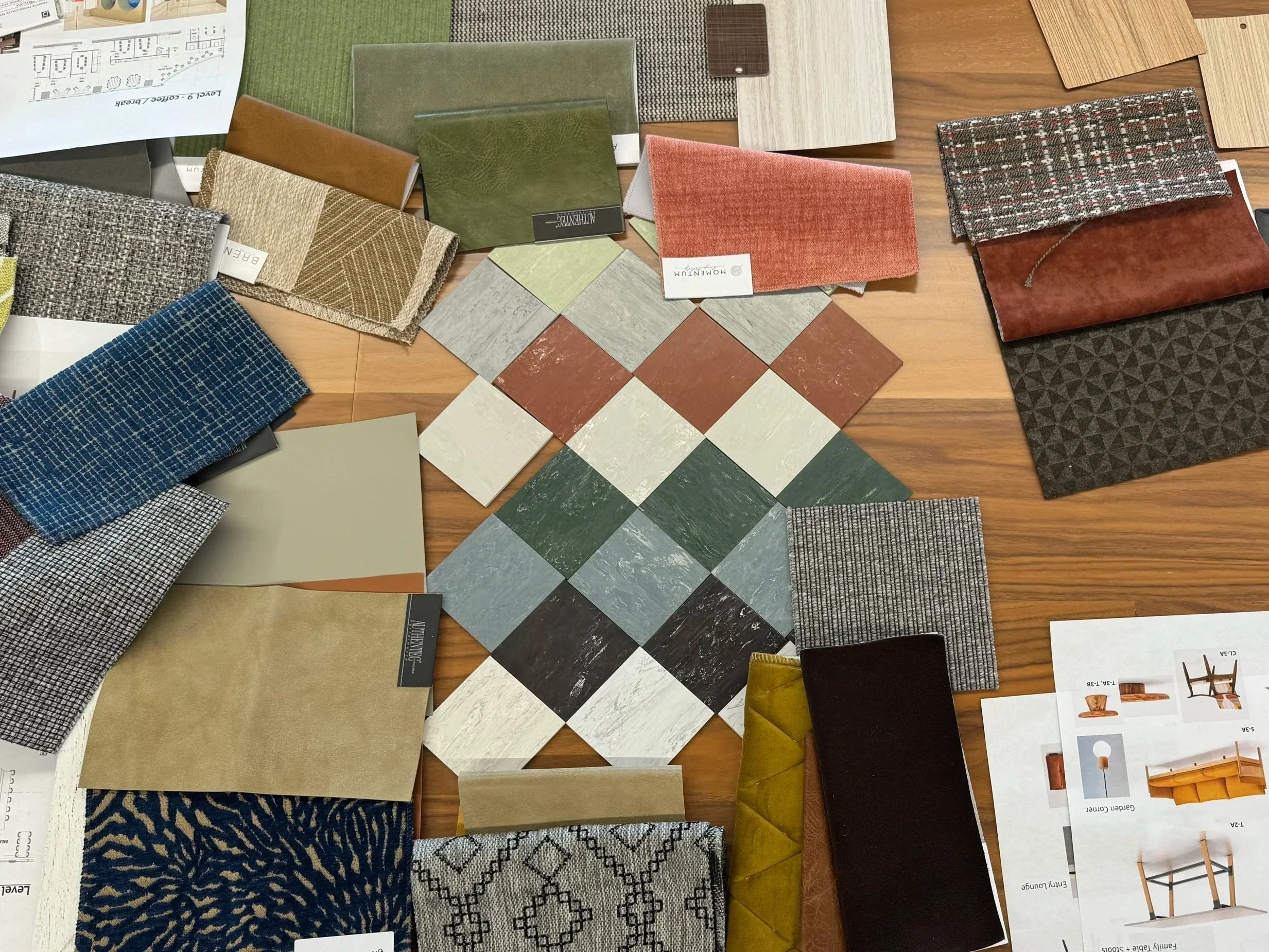A collection of fabric swatches, color samples, and design samples for interior decorating or furniture upholstery displayed on a wooden table.