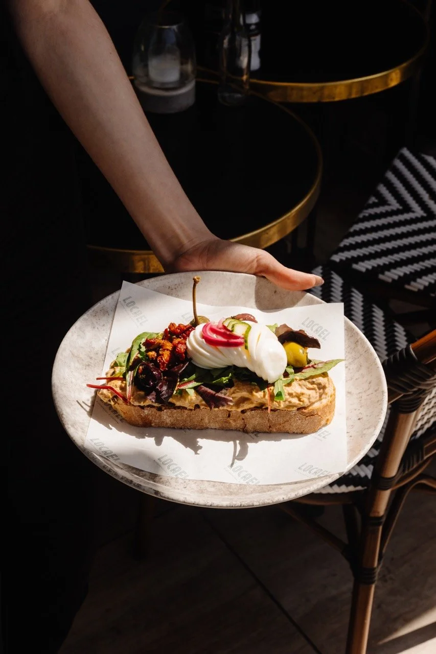 Sandwich met sla, ham, kaas en tomaat op een bord, inclusief een glas sinaasappelsap en drie glazen water op een tafel.