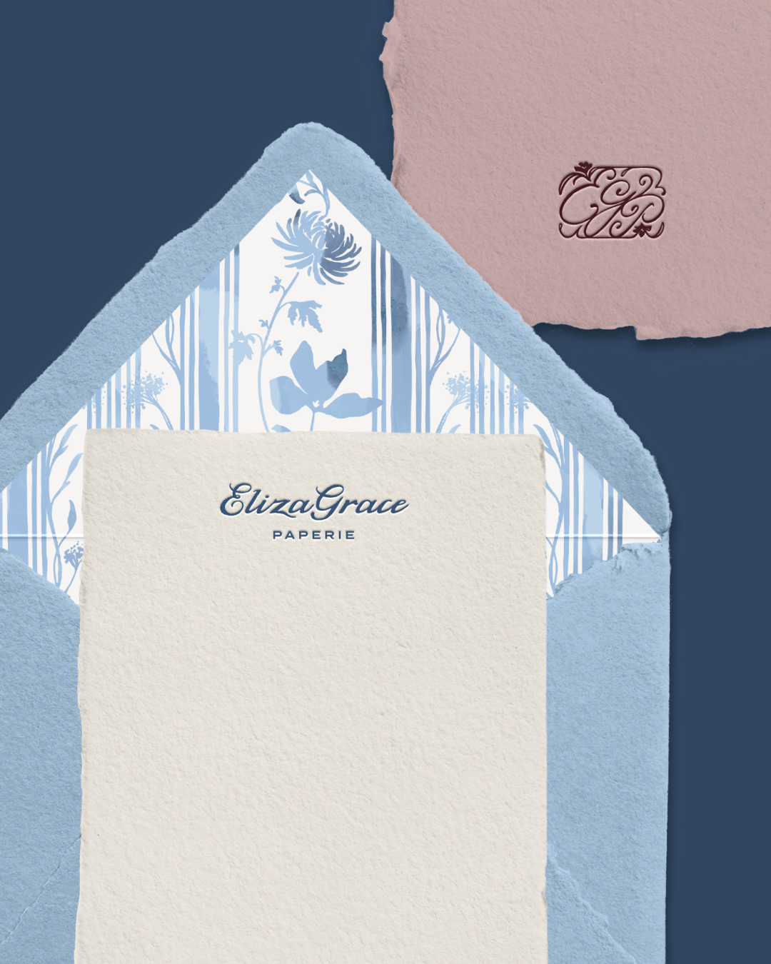 A light blue envelope with a floral liner sits partially open, revealing a cream sheet printed with “Eliza Grace Paperie,” with a mauve monogrammed paper in the corner.