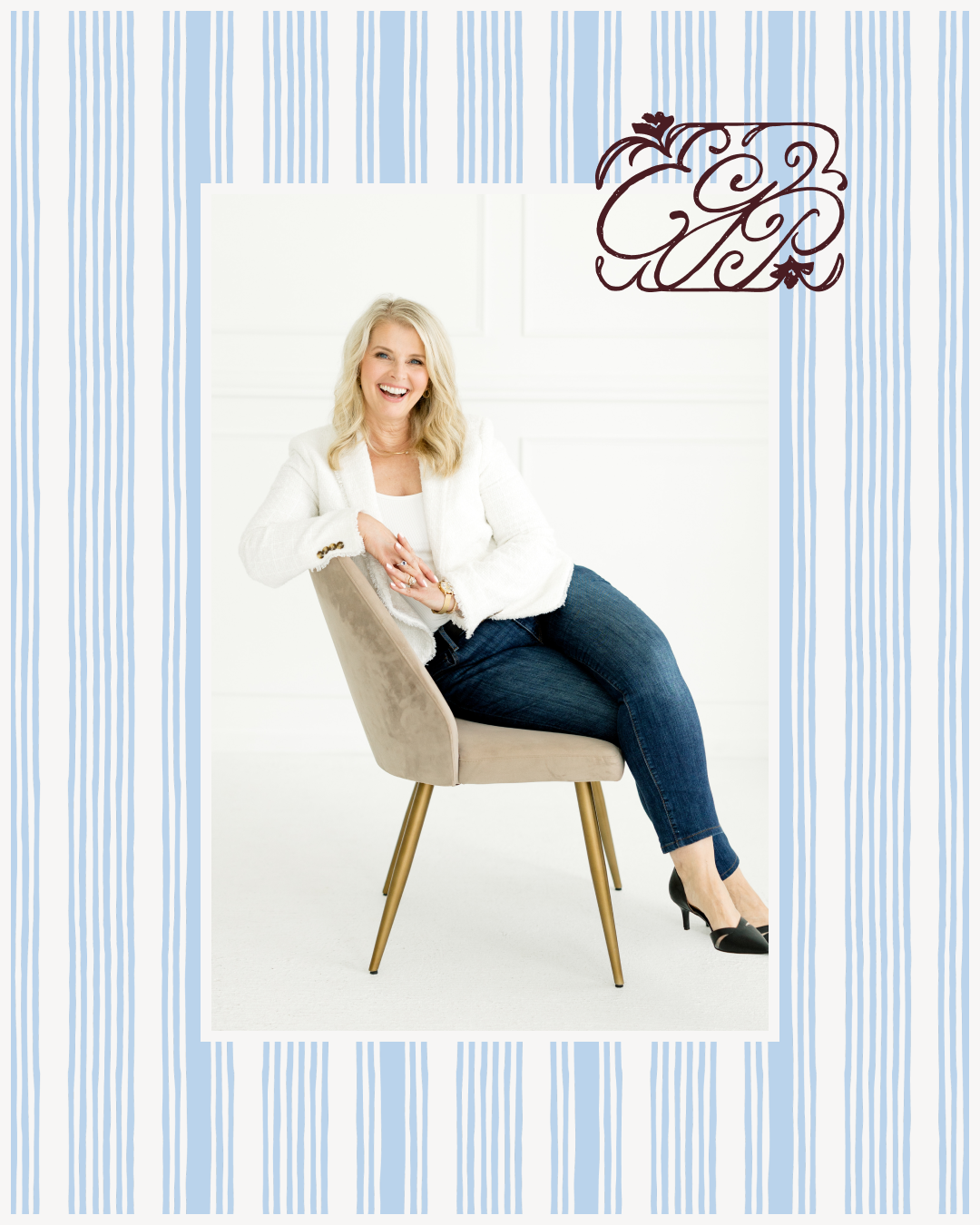 A person seated on a beige chair in a bright white room, wearing a white textured blazer, dark jeans, and black heels. A decorative monogram appears in the upper corner against a striped blue border.