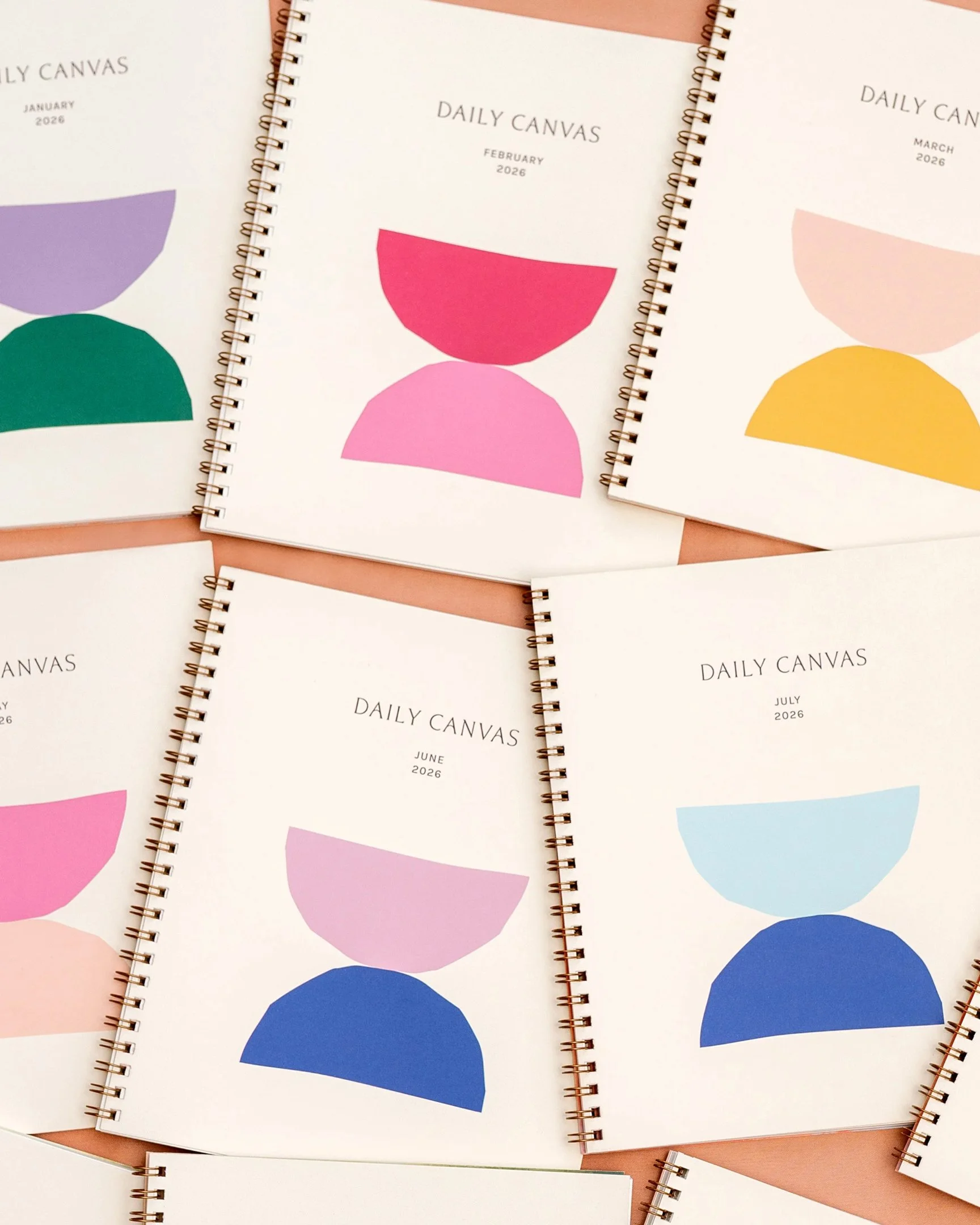 Collection of Daily Canvas spiral-bound monthly planners fanned out, showcasing colorful geometric cover designs created by Solmade Studio.