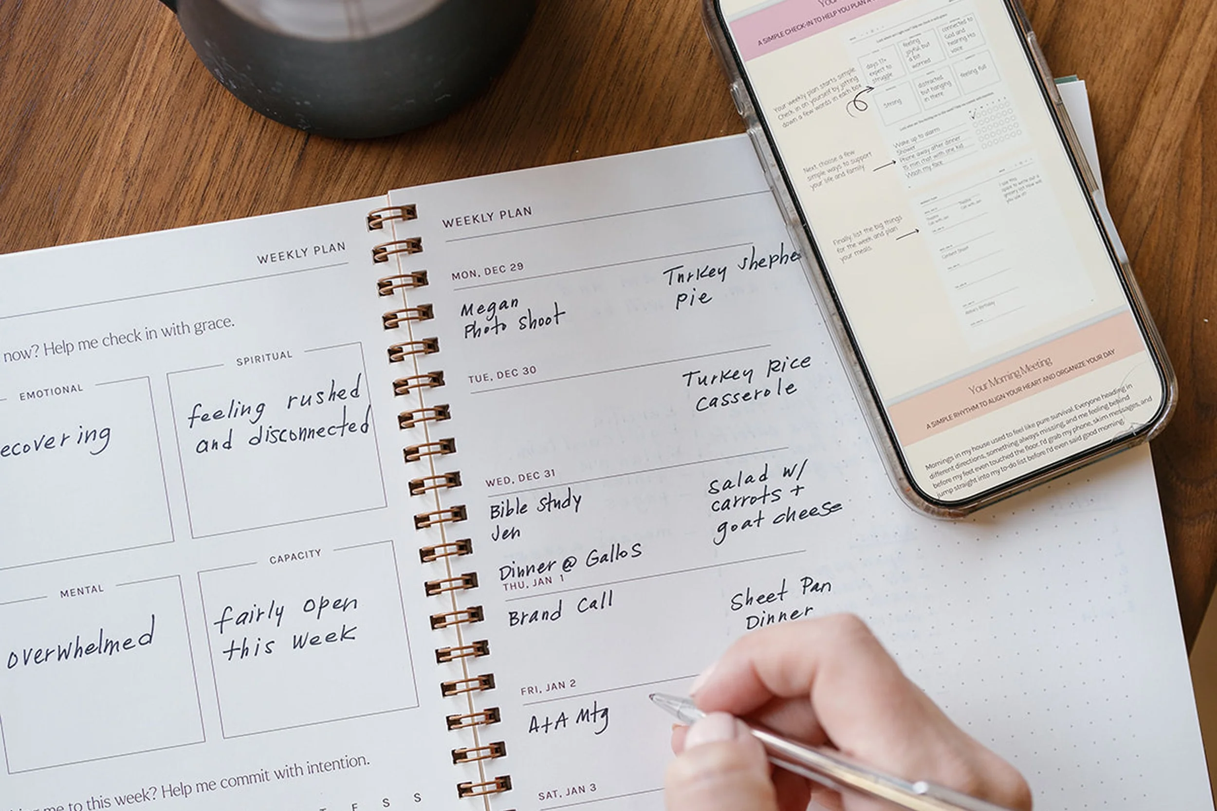 Overhead view of an open Daily Canvas planner showing handwritten weekly schedules next to a smartphone displaying the planner’s digital companion.