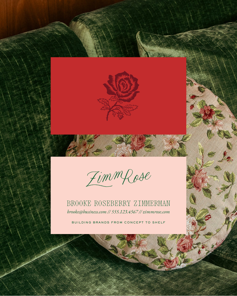 Two ZimmRose business cards placed on a green velvet couch: a red card with a rose illustration and a pink card with contact information for Brooke Roseberry Zimmerman, styled with elegant typography and a tagline