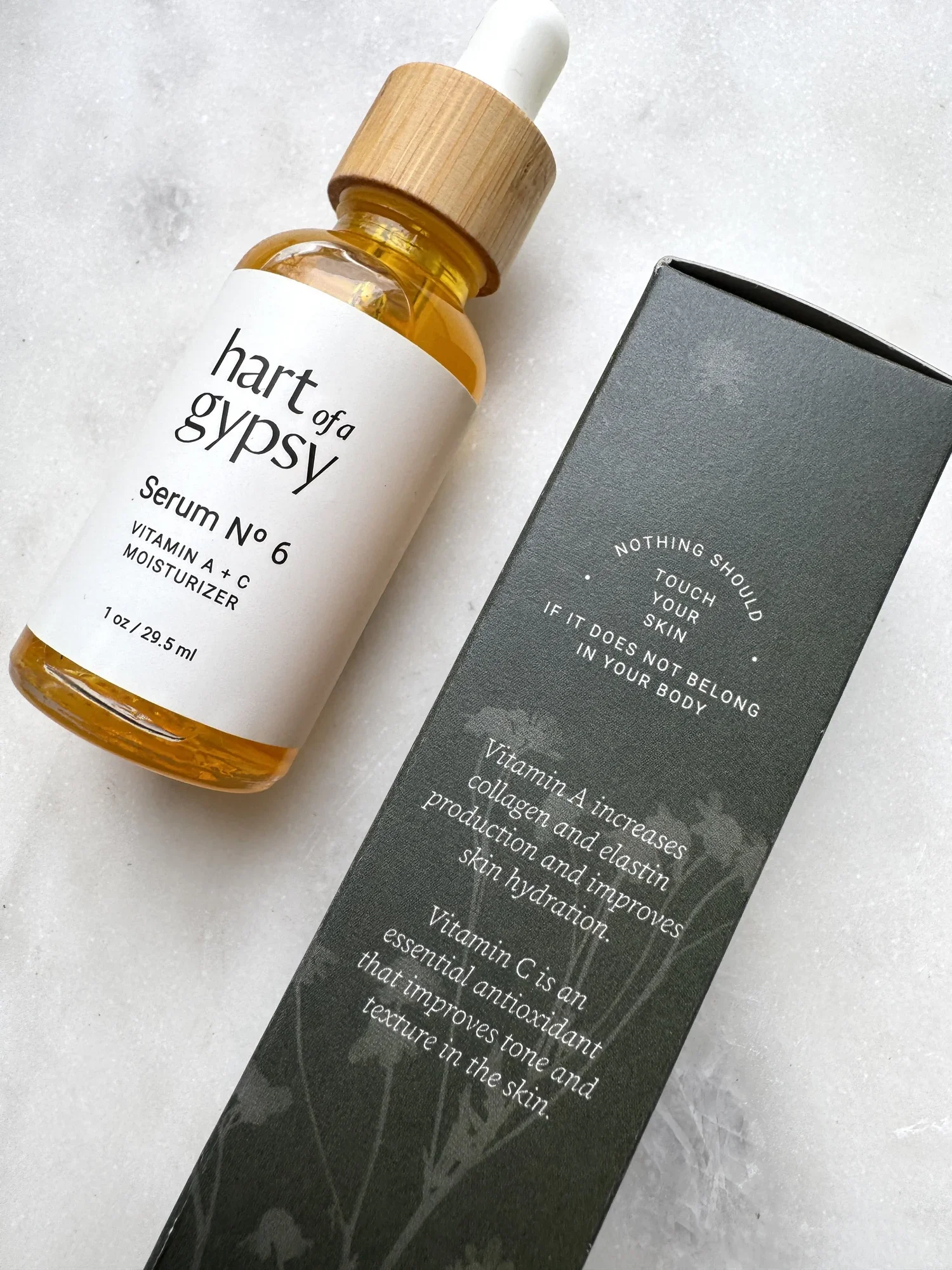 Amber glass dropper bottle labeled “hart of a gypsy Serum No. 6 Vitamin A + C Moisturizer” beside a dark gray box with product benefits printed in white.