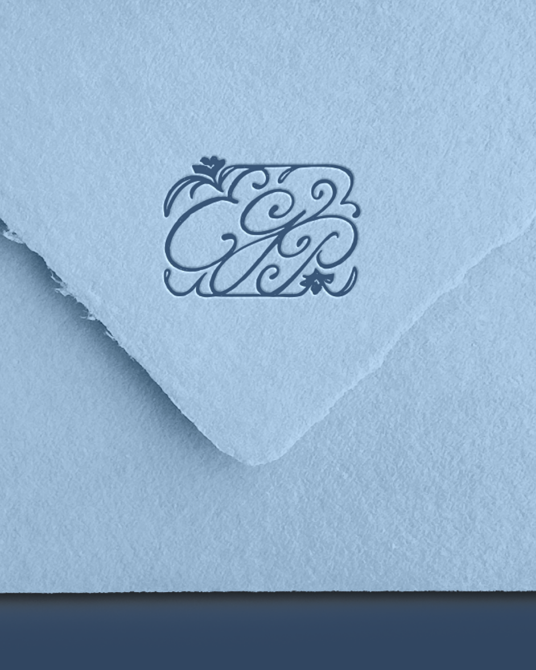 A close-up of a textured light blue envelope with an ornate “ECP” monogram on the flap, decorated with delicate floral flourishes that highlight the brand’s handcrafted stationery style.