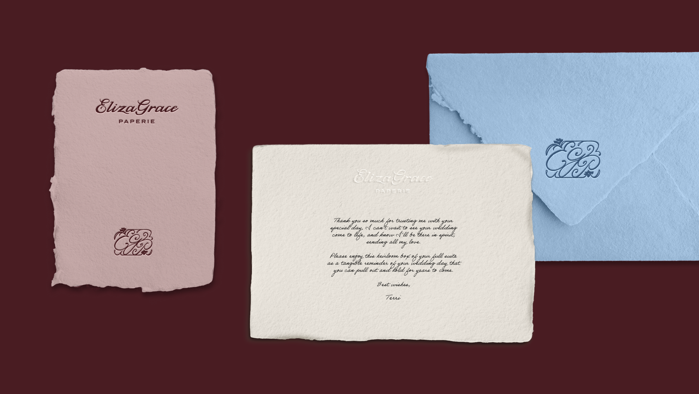 A pink card, cream card, and light blue envelope arranged on a maroon background, each featuring ElizaGrace Paperie branding and matching monograms.