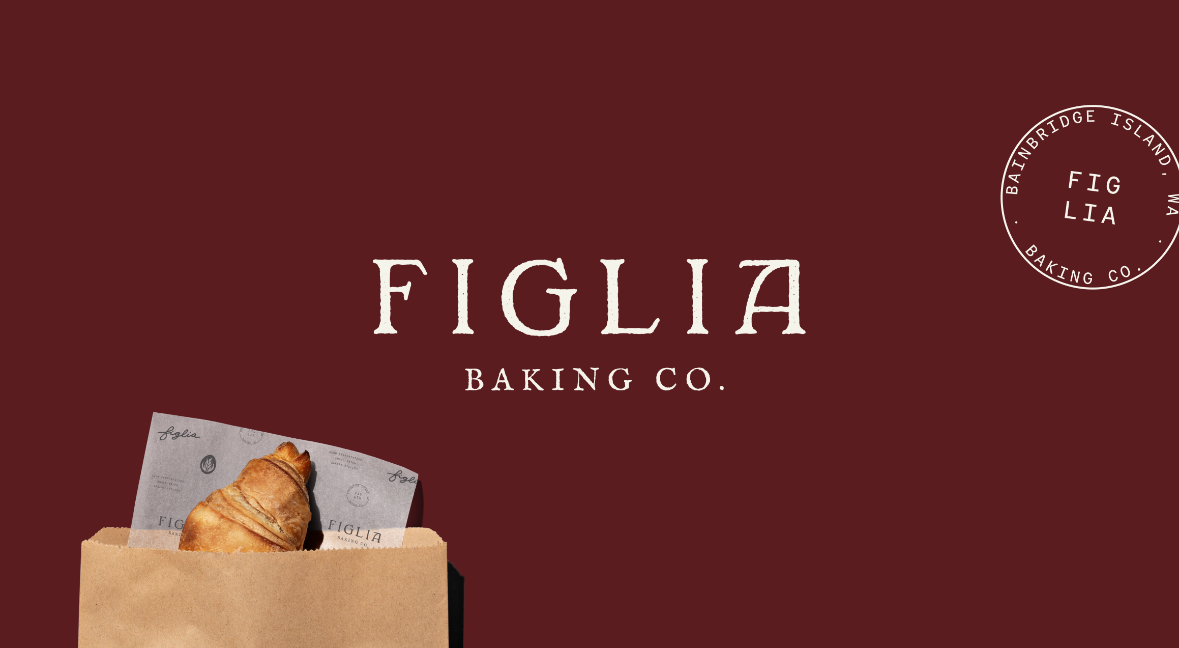 A croissant in a brown Figlia Baking Co. paper bag sits on a dark maroon background. A circular Figlia logo appears in the upper right corner, featuring a wheat emblem and “Bainbridge Island, WA.