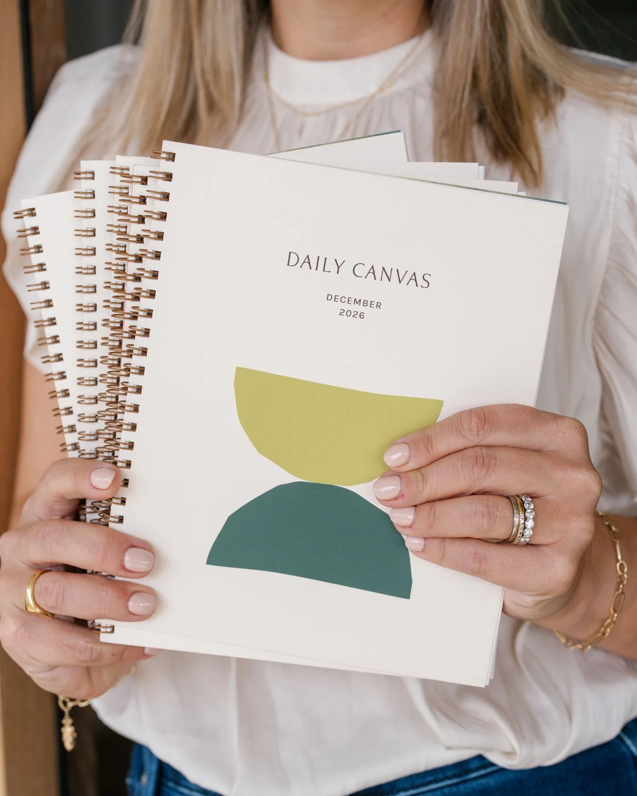 Woman holding the December edition of the Daily Canvas planner featuring a minimalist cream cover with abstract shapes..