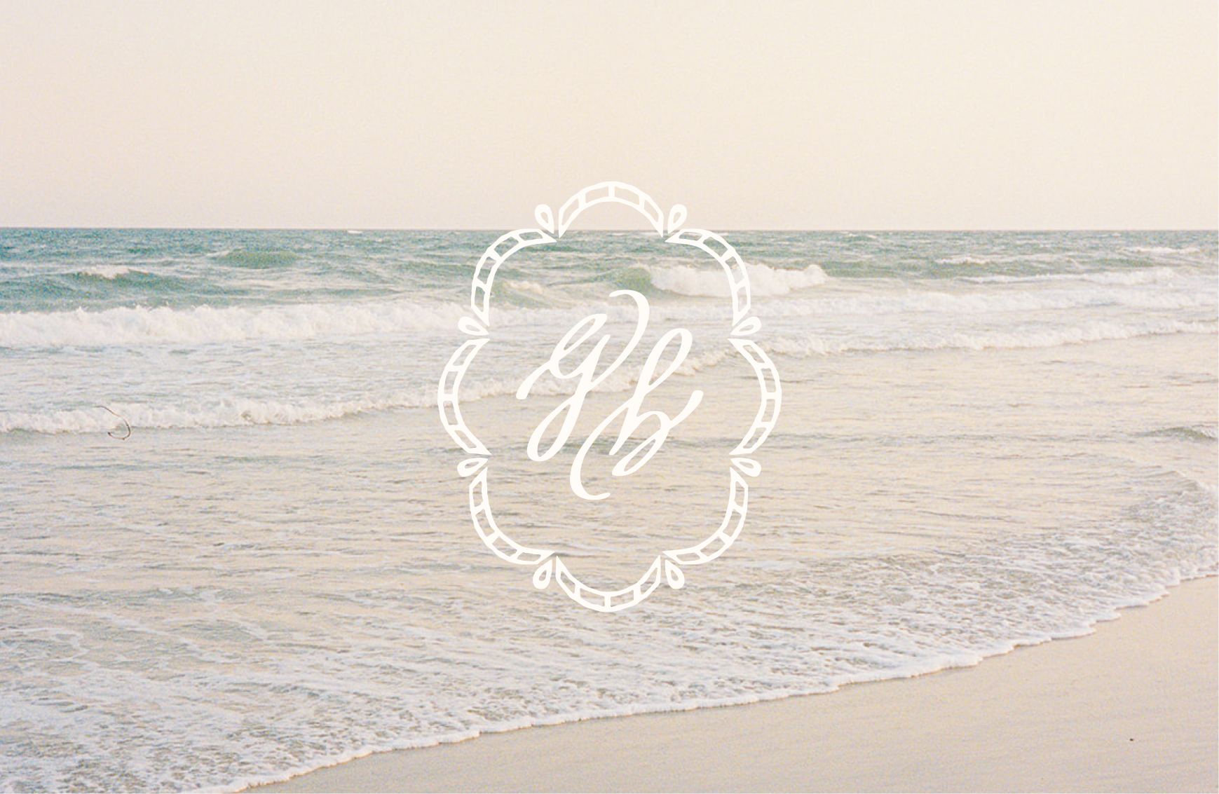 A calm beach with gentle waves under a pastel sky. Centered is an ornate white emblem featuring stylized cursive letters.