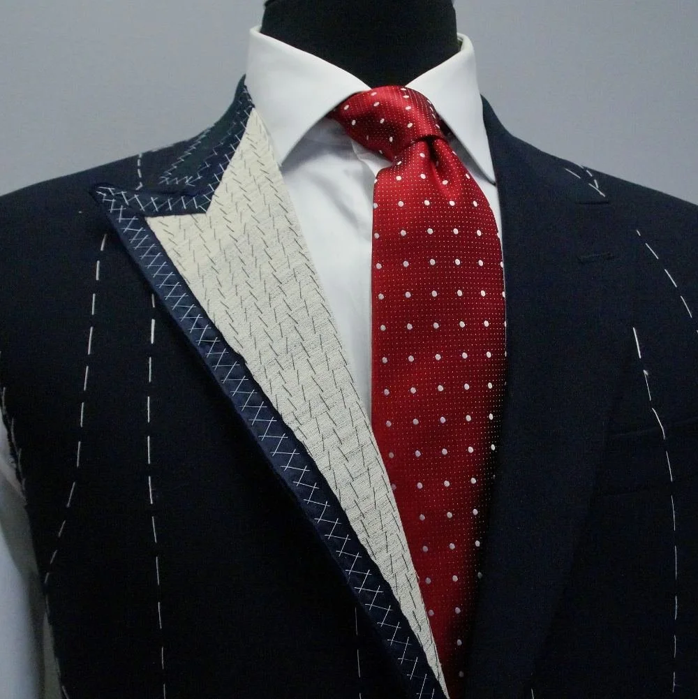 Half-finished navy suit showing inner construction with white stitching on mannequin.