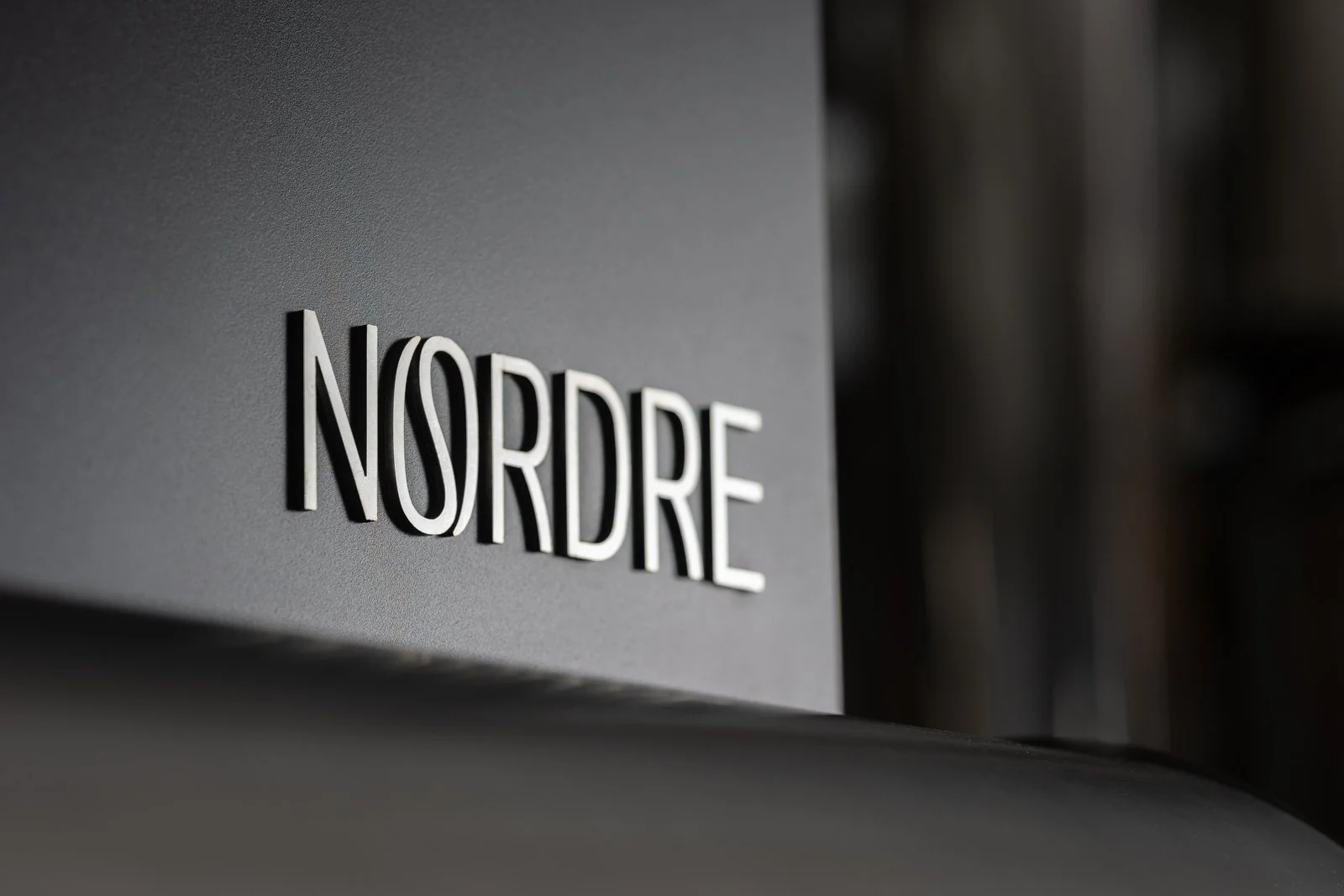 NORDRE logo in white 3D letters on a charcoal surface