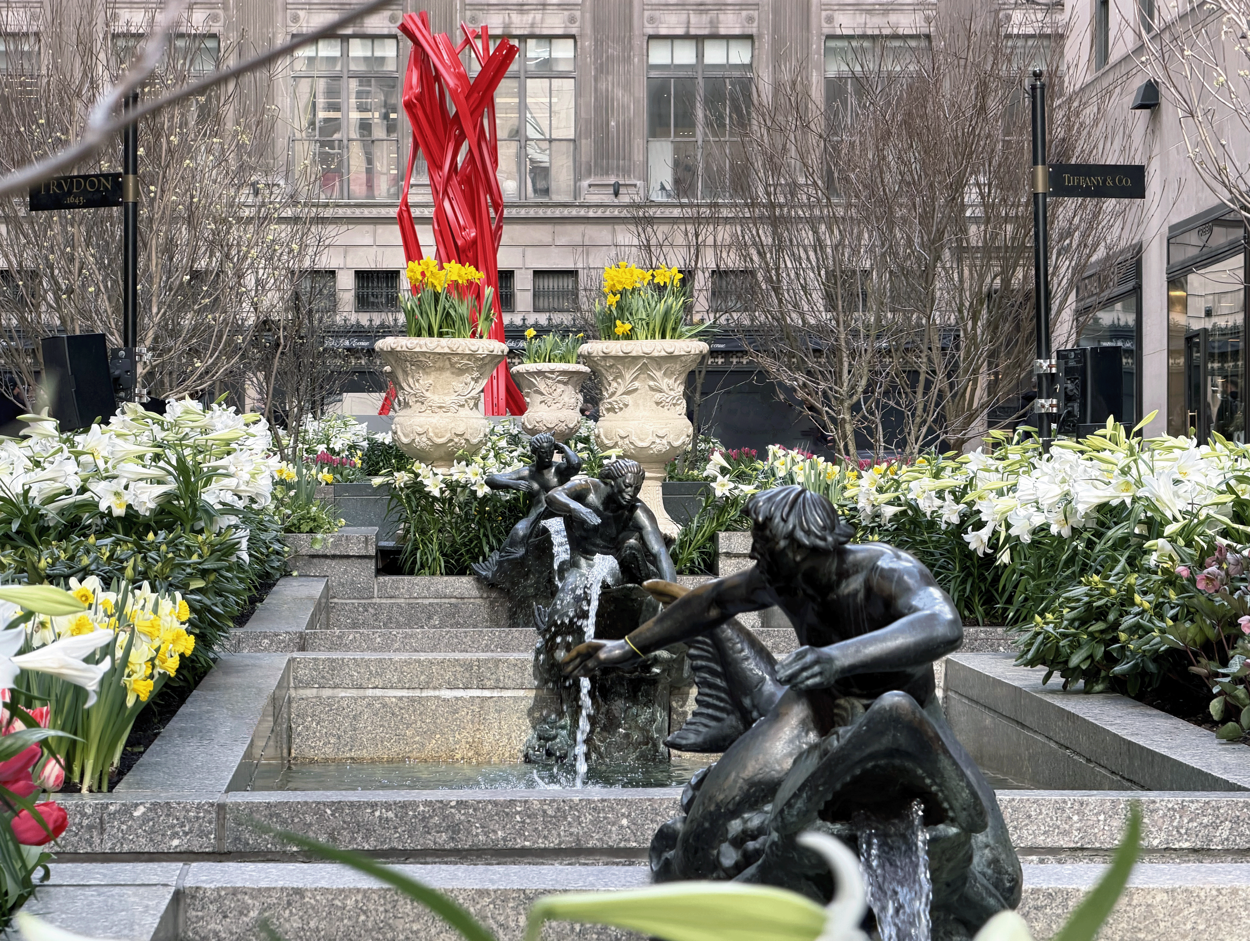 Channel Gardens at Rockefeller Center contains beautiful flower beds, trees, statues, and a marble fountain, surrounded by historical high-rise buildings in the heart of NYC. 
