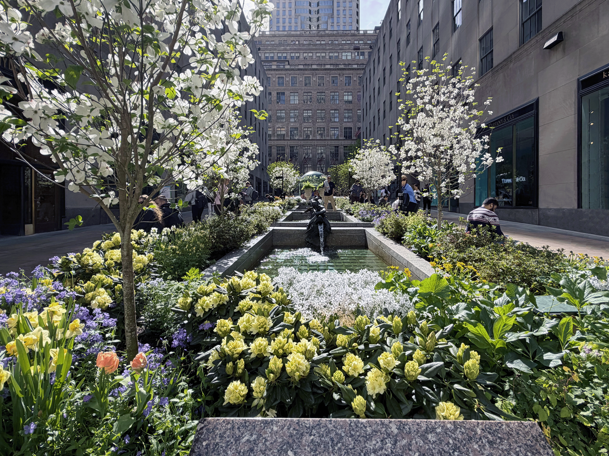 Channel Gardens at Rockefeller Center contains beautiful flower beds, trees, statues, and a marble fountain, surrounded by historical high-rise buildings in the heart of NYC. 