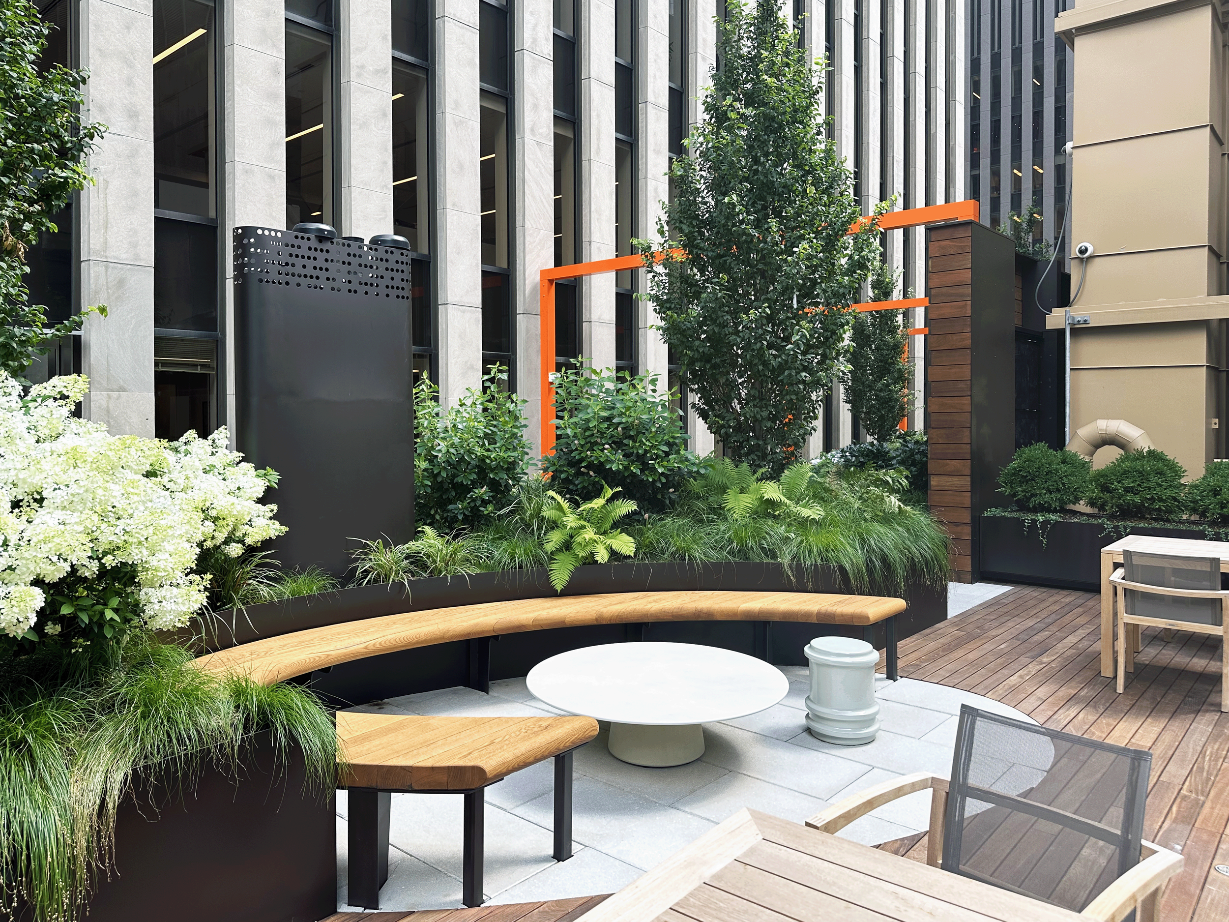 Urban outdoor patio with modern seating, lush greenery, and high-rise buildings in the background.