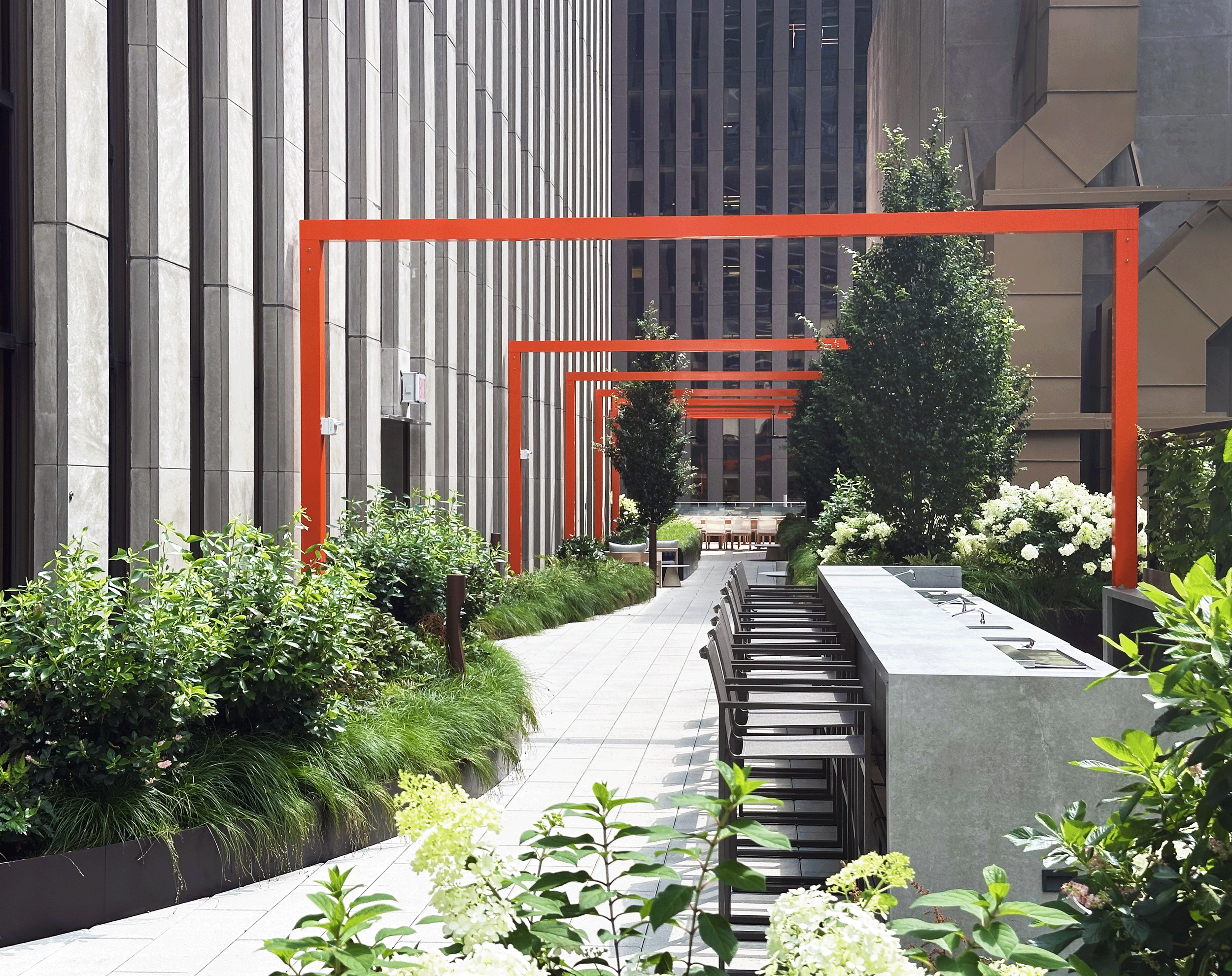 Modern outdoor rooftop terrace with orange metal arches, lush green plants, trees, and a seating area.
