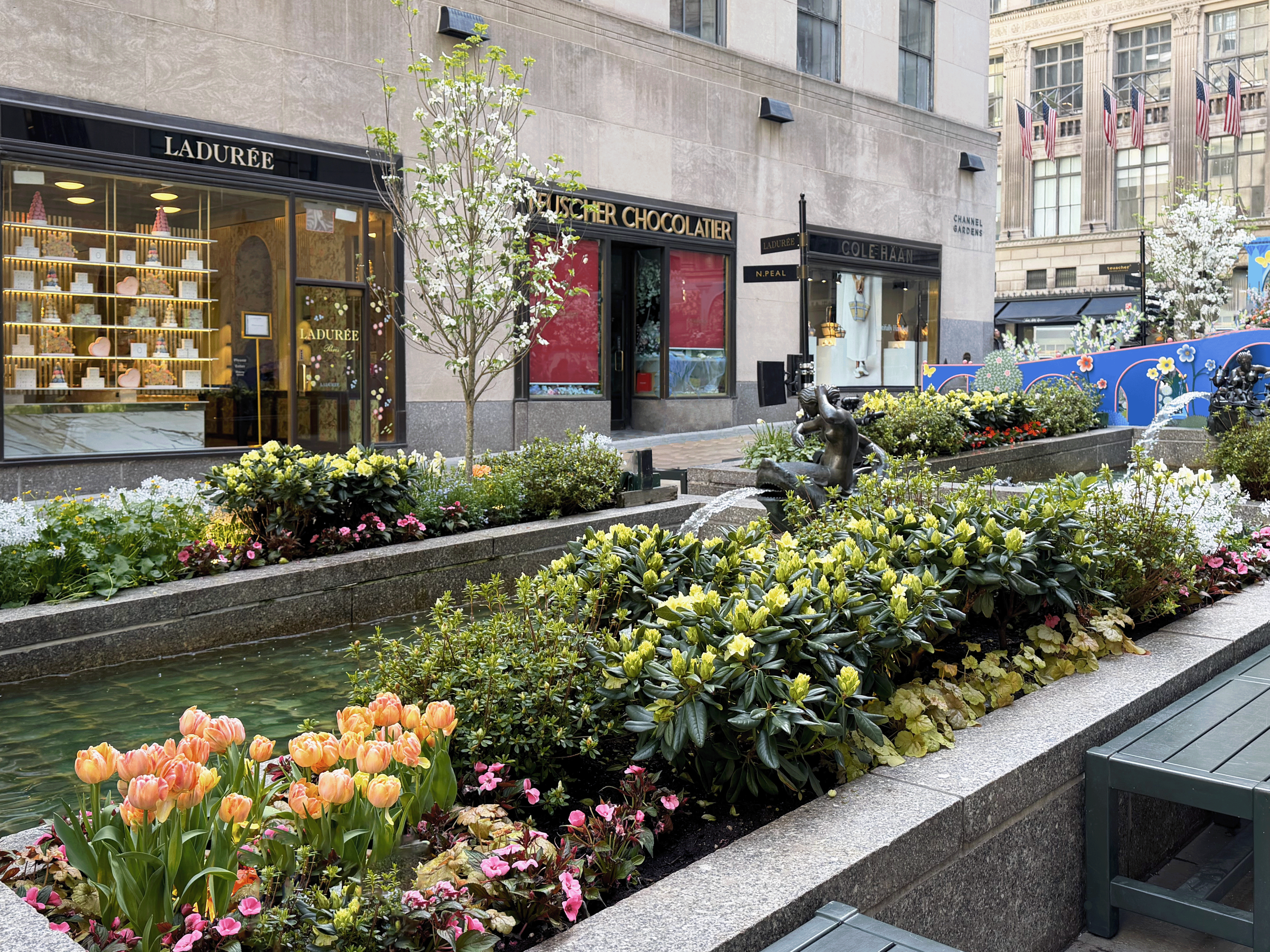 Channel Gardens at Rockefeller Center contains beautiful flower beds, trees, statues, and a marble fountain, surrounded by historical high-rise buildings in the heart of NYC. 
