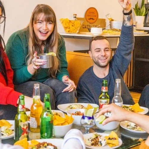 Friends enjoying a Big Game watch party with Local Cantina taco bar catering, featuring party pack tacos, tortilla chips, and drinks in a casual at-home setting.