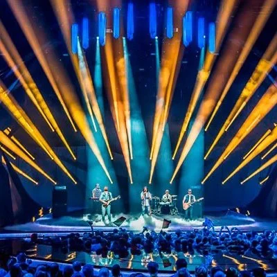 A live concert with a band performing on stage under colorful lights, with an audience watching.